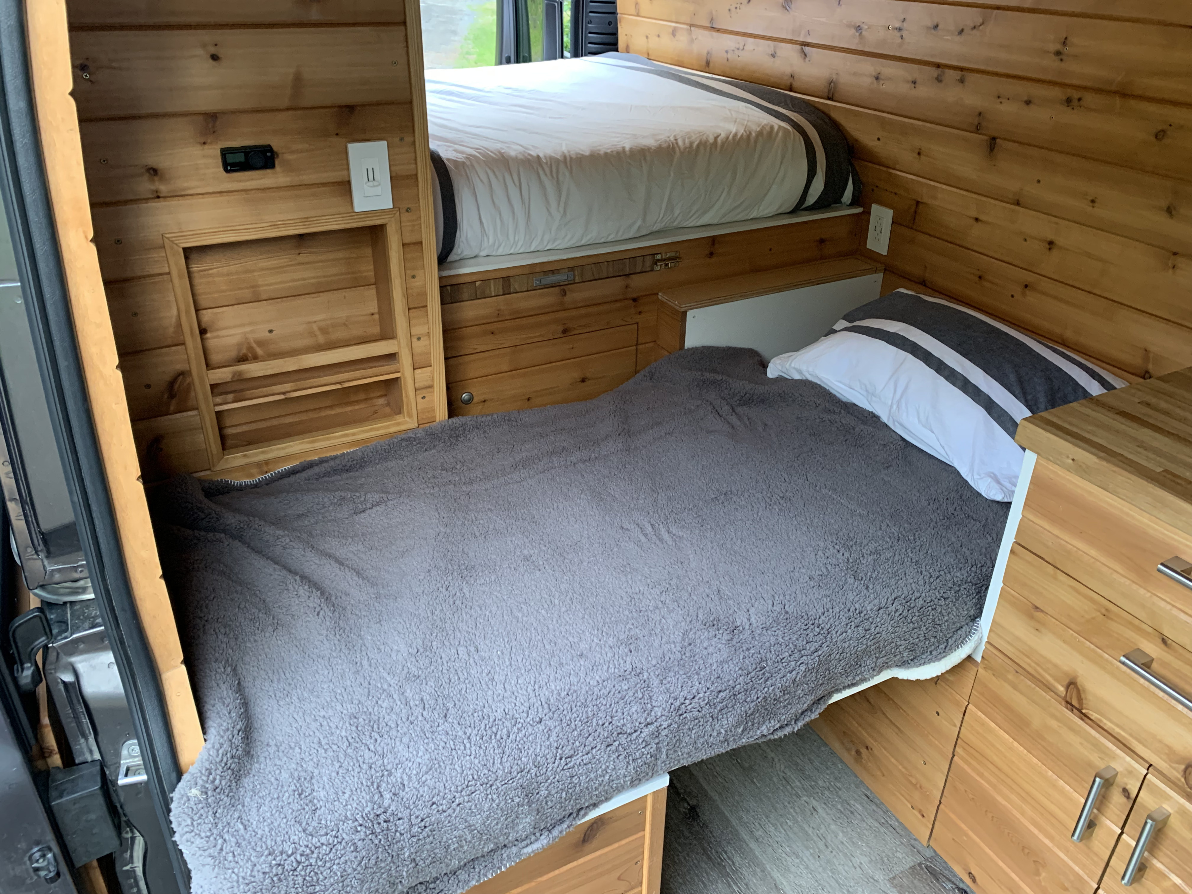 Inside an RV rental: a compact, wood-paneled sleeping area with comfortable bunk beds and clever storage.. Dodge Van 2024