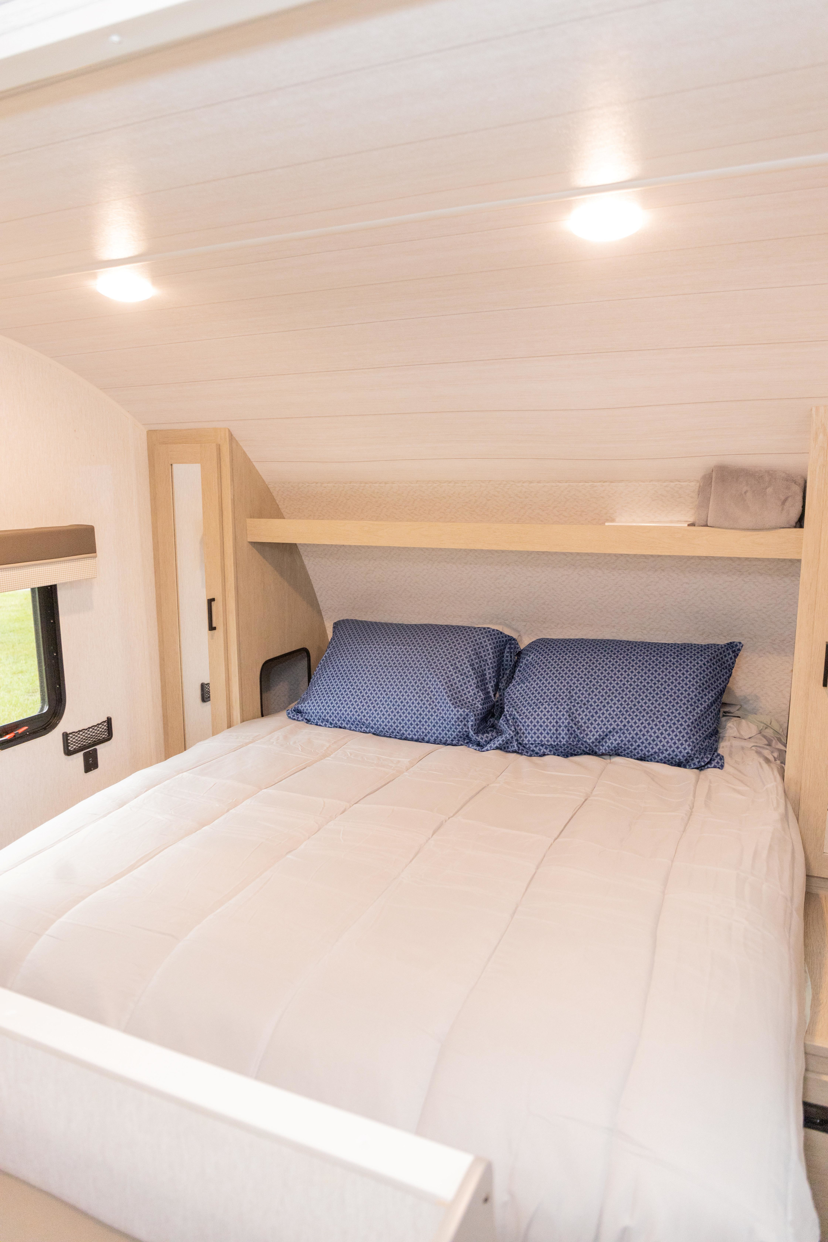 Cozy RV rental bedroom with light wood walls, a comfortable bed, and overhead storage. Ideal for travel.. Forest River Salem Cruise Lite 2023
