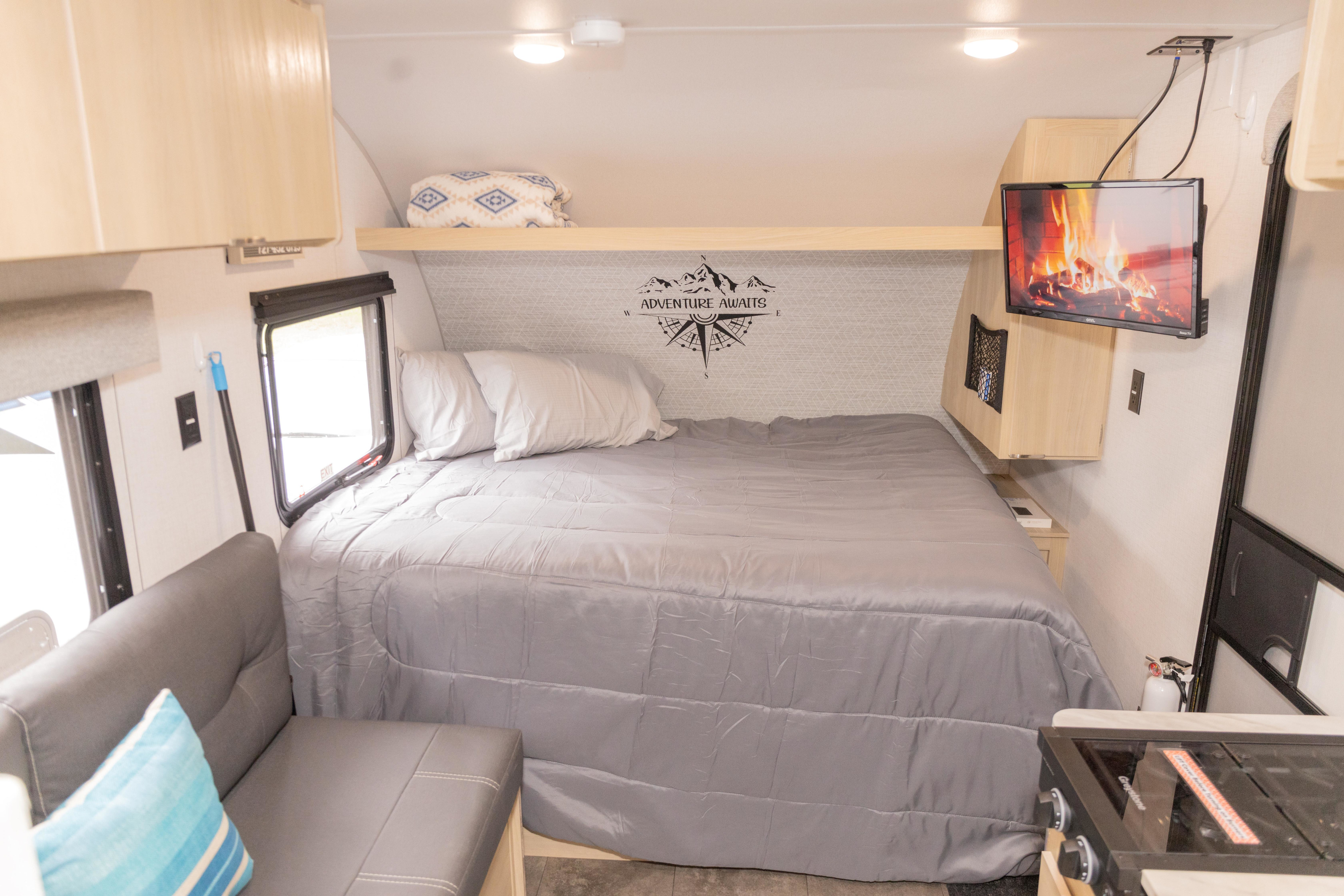 This rv rental features a comfortable bed with 'ADVENTURE AWAITS' wall art, a TV, and a small seating area.. Forest River Salem FSX 2024