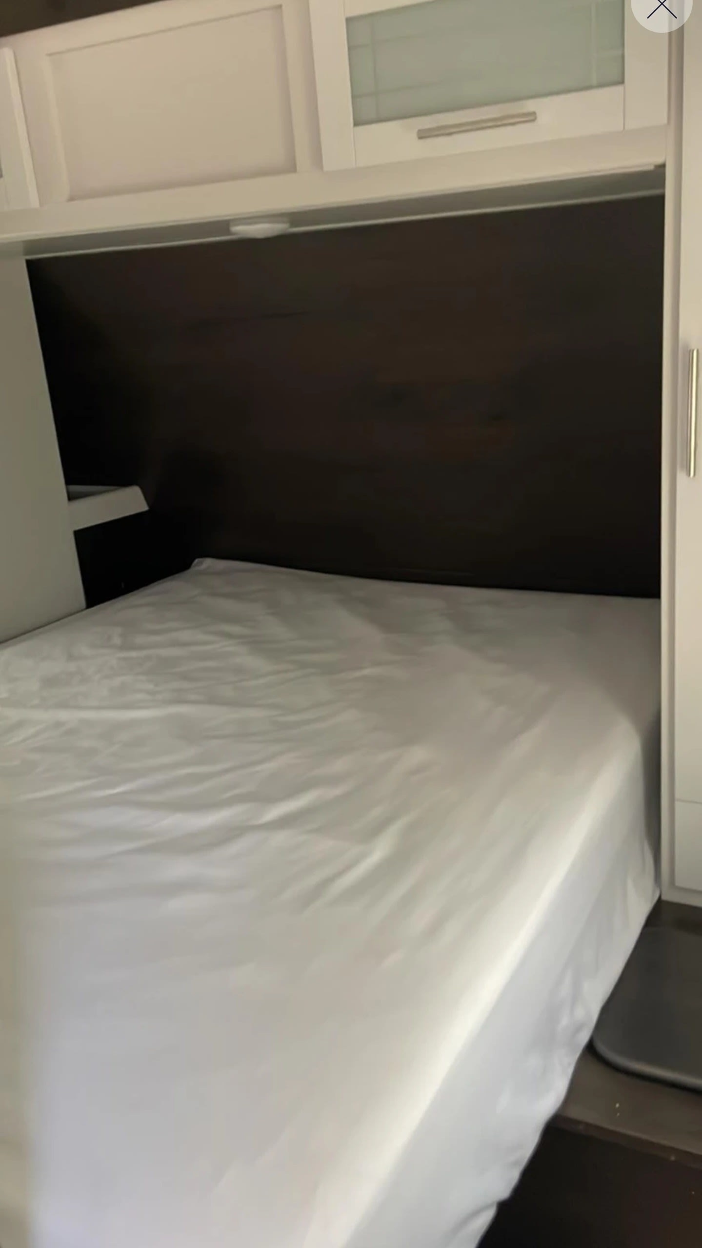 Visually, a clean white bed fills an RV rental sleeping nook, featuring overhead cabinets & dark wood paneling.. Keystone RV Bullet Ultra Lite 2021