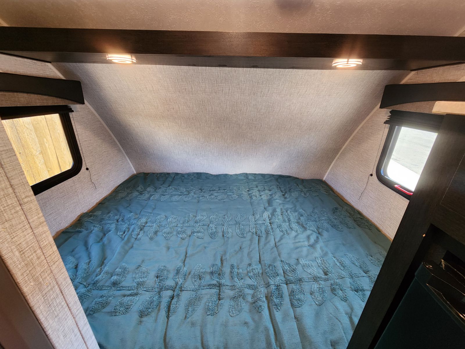 Cozy RV rental bedroom with a teal comforter and overhead lighting, perfect for your next adventure.. Braxton Creek Bushwhacker Plus 2022