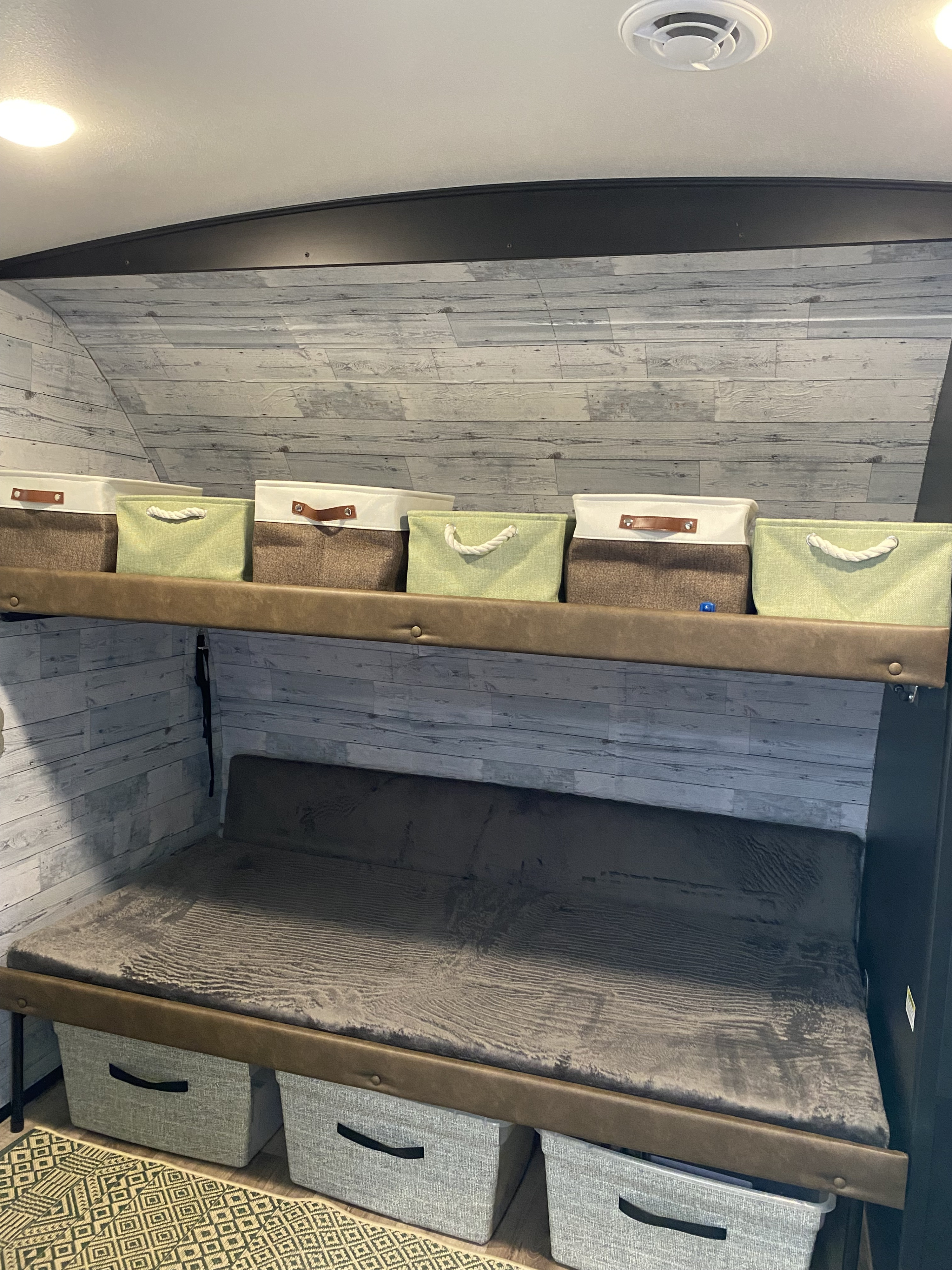 Inside an **RV rental**: a cozy bunk area with stylish wood-look walls, ample storage bins, and a plush bed.. Keystone Outback 2022