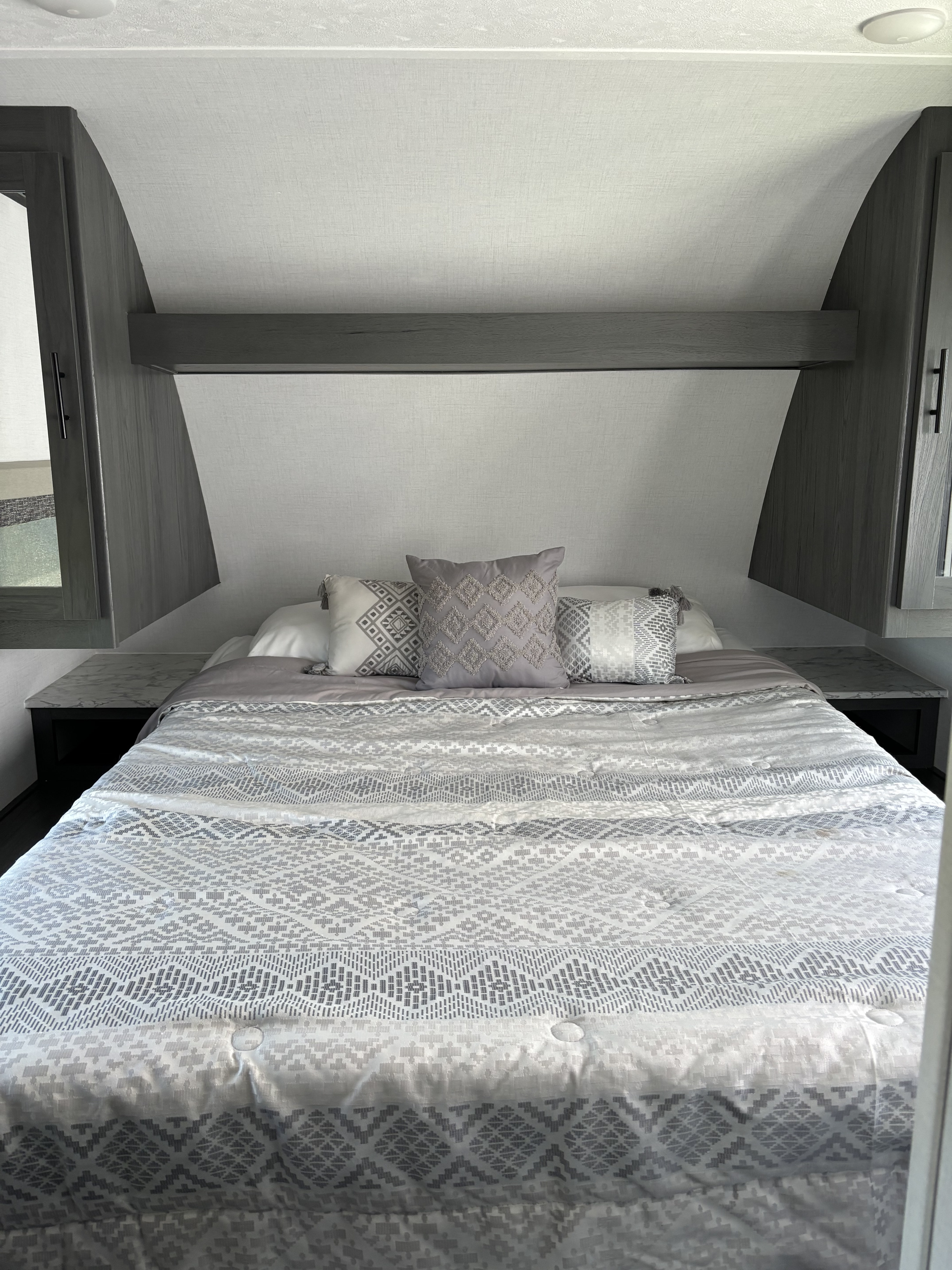 Cozy RV rental bedroom features a comfy bed with modern gray patterned bedding, decorative pillows, and built-in storage cabinets.. Dutchmen Colorado Series 2024
