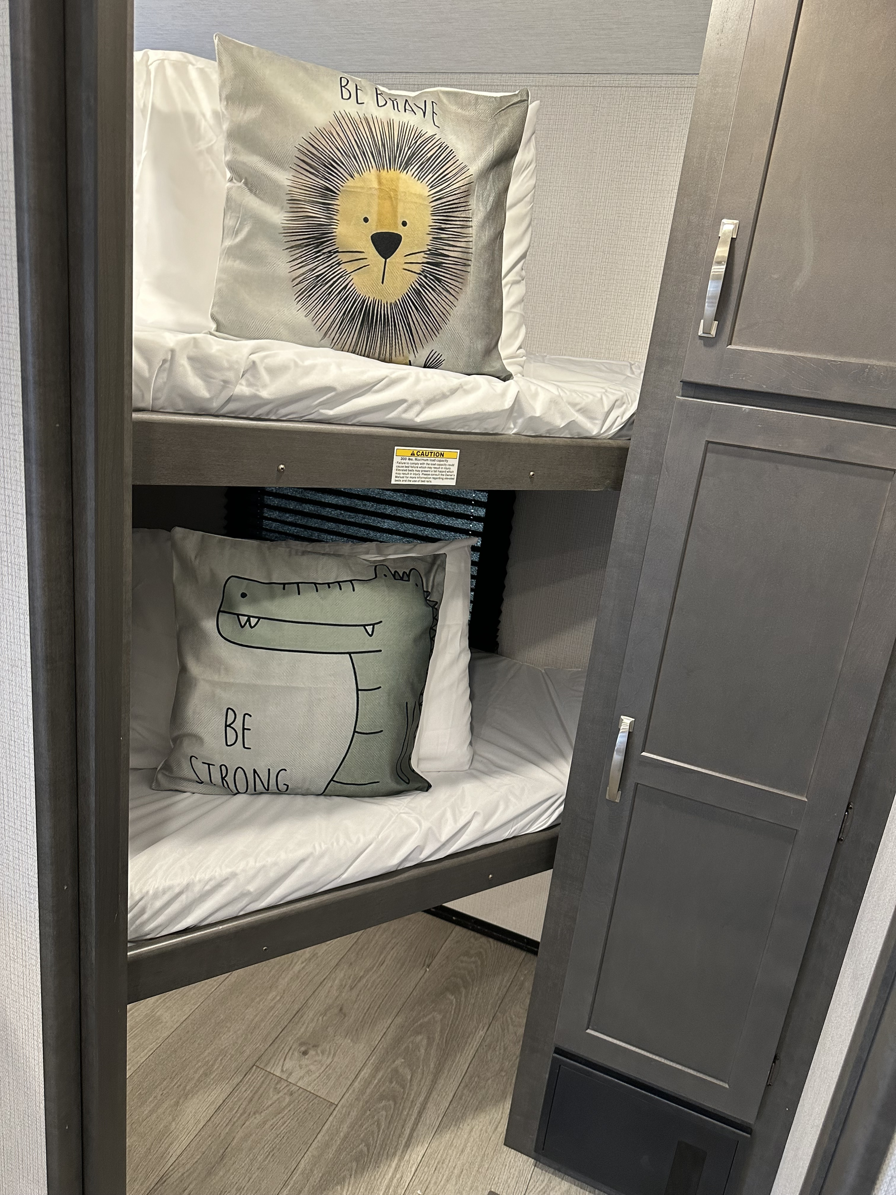 An RV rental's cozy bunk beds, featuring "Be Brave" lion and "Be Strong" crocodile pillows, ready for young adventurers.. Keystone Cougar Sport 2700BH 2024