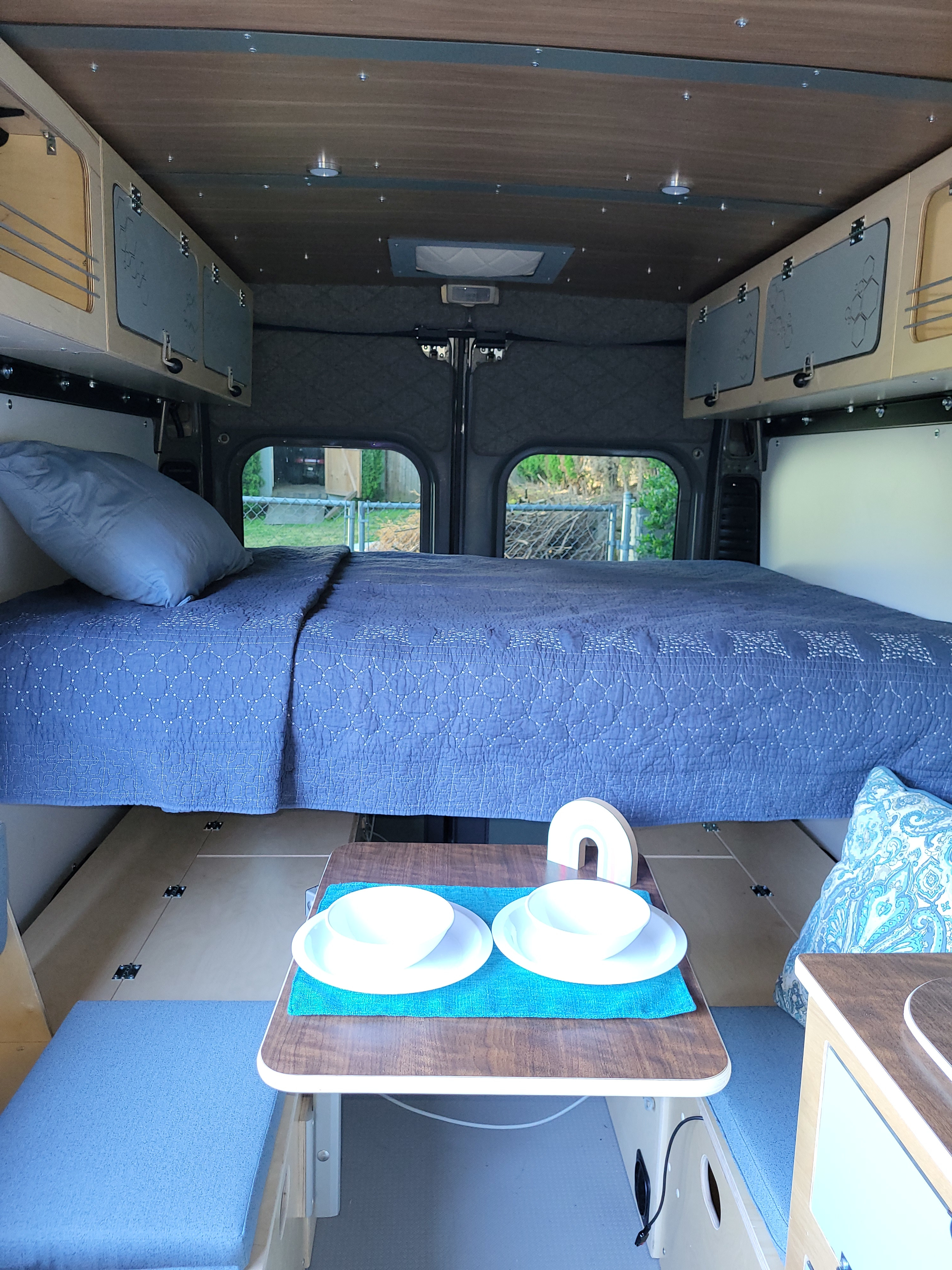 Cozy RV rental interior with a comfy bed, dinette, and storage. Perfect for mobile living adventures.. Custom Ram Promaster 2023