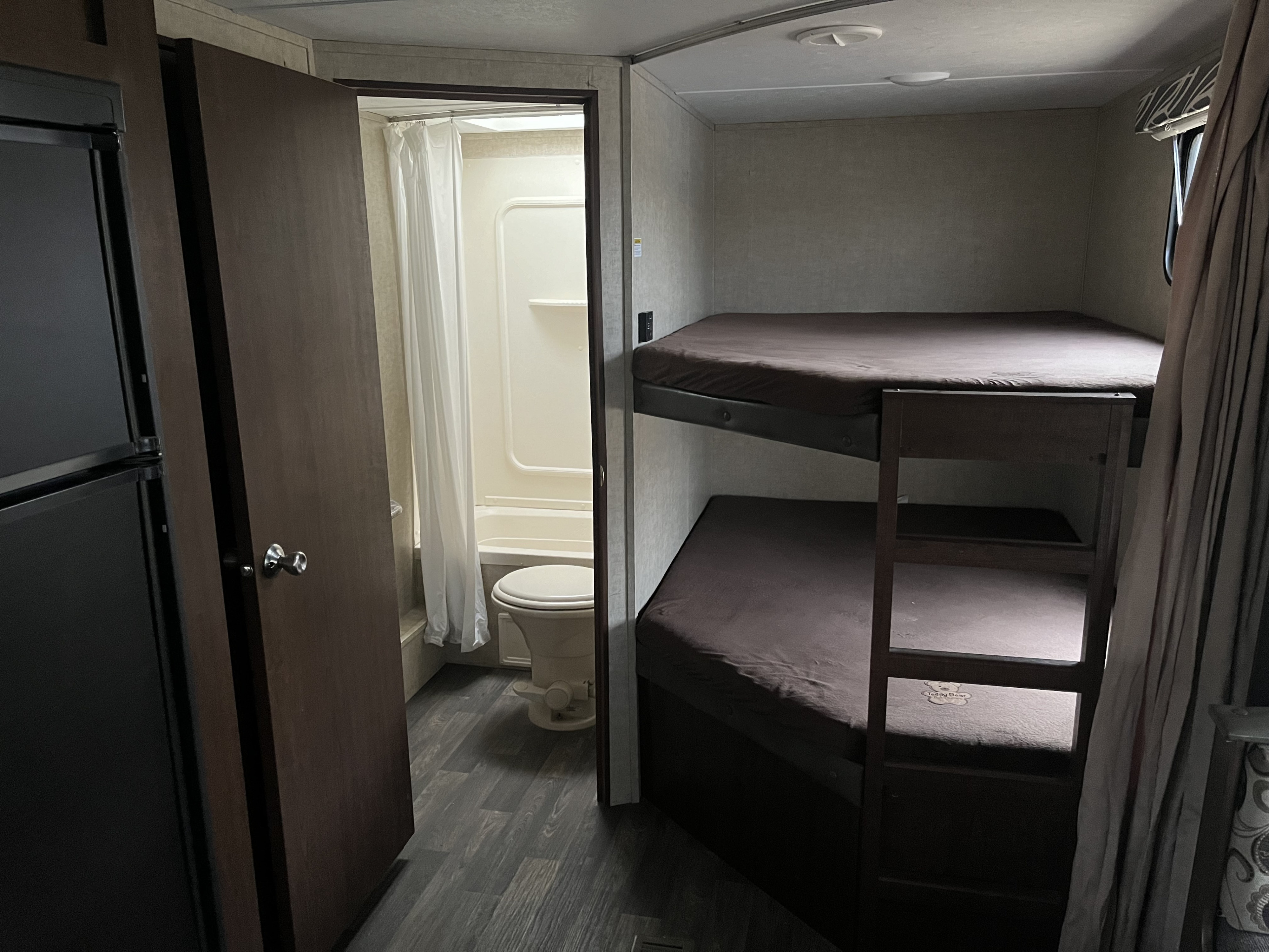 RV rental interior featuring dark brown bunk beds, a compact bathroom with a shower and toilet, and a refrigerator.. Keystone RV Hideout LHS 2016