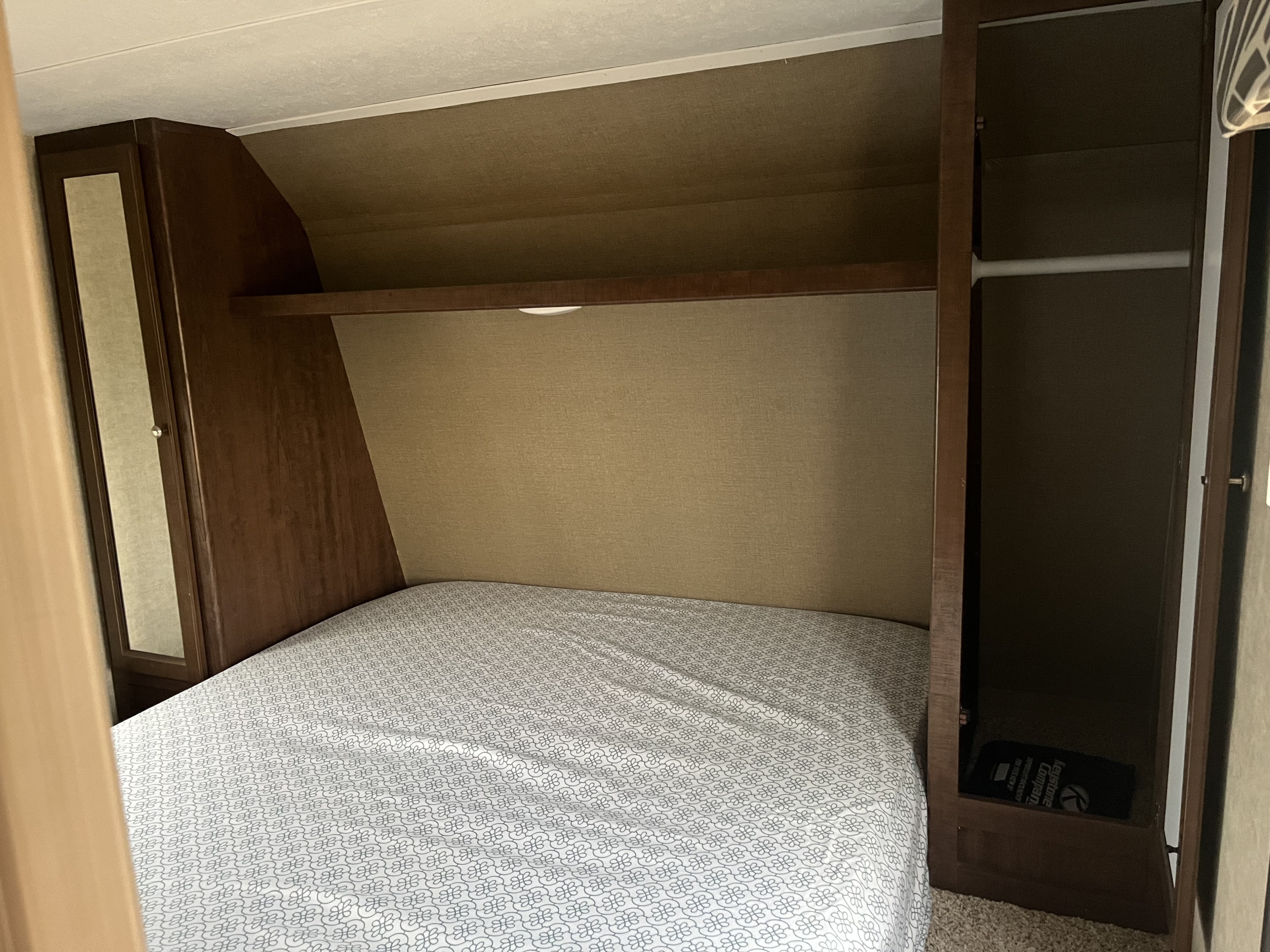 Inside an RV rental: a compact bedroom with a patterned bed, built-in shelf, and wardrobe storage.. Keystone RV Hideout LHS 2016