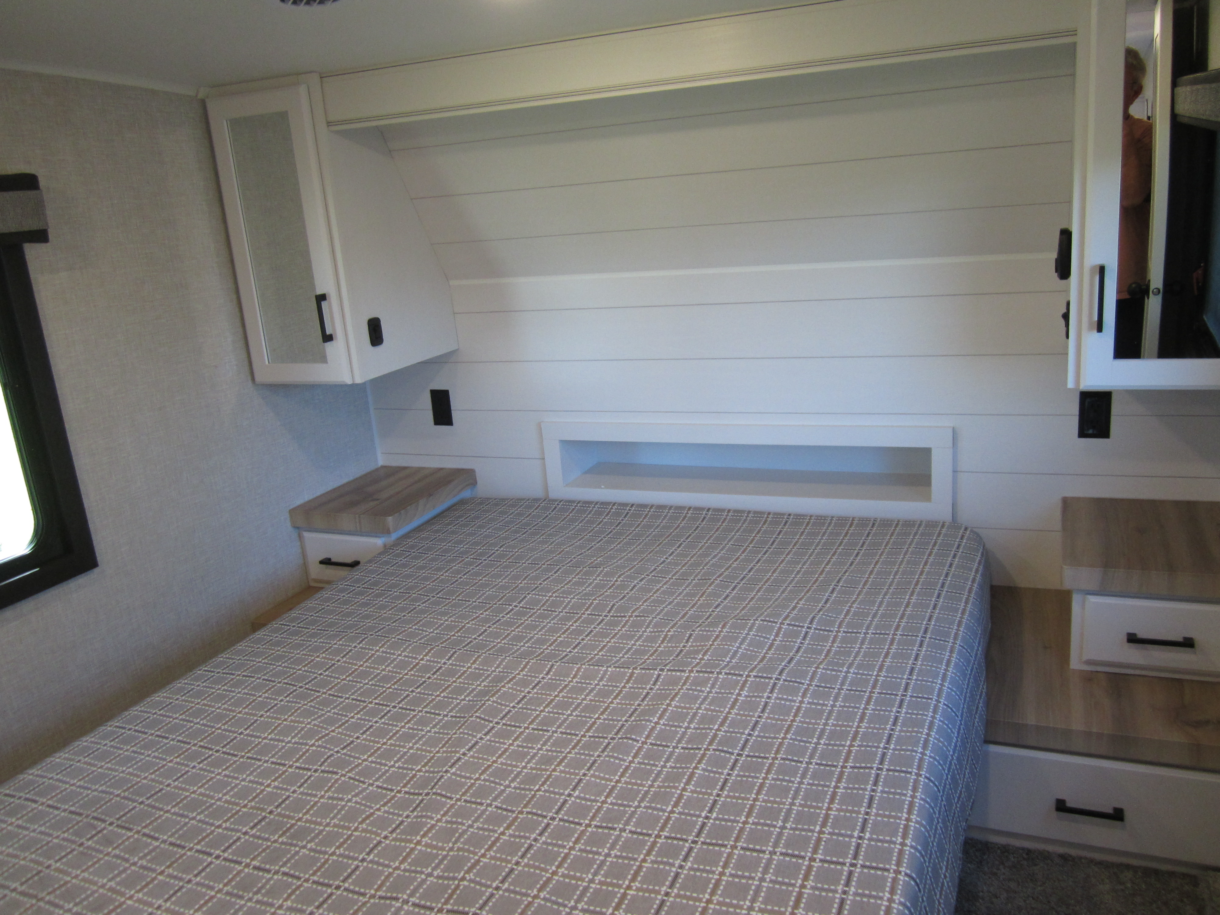 Cozy RV rental bedroom features a plaid bedspread, modern shiplap headboard, and built-in storage.. Jayco Eagle HT 2024