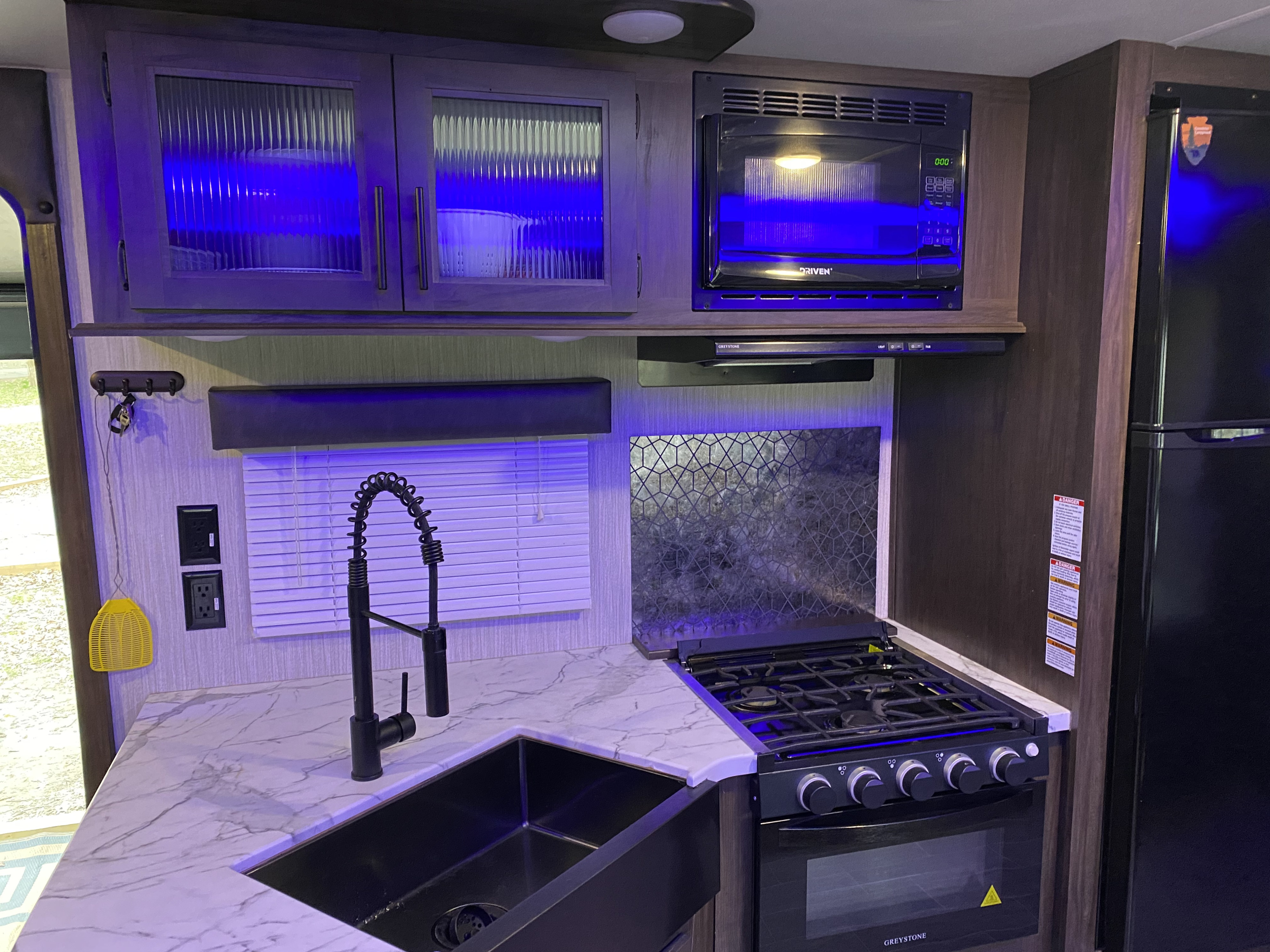 Modern RV rental kitchen with striking blue accent lights, featuring microwave, stove, and sink.. Forest River Cherokee Grey Wolf 2021
