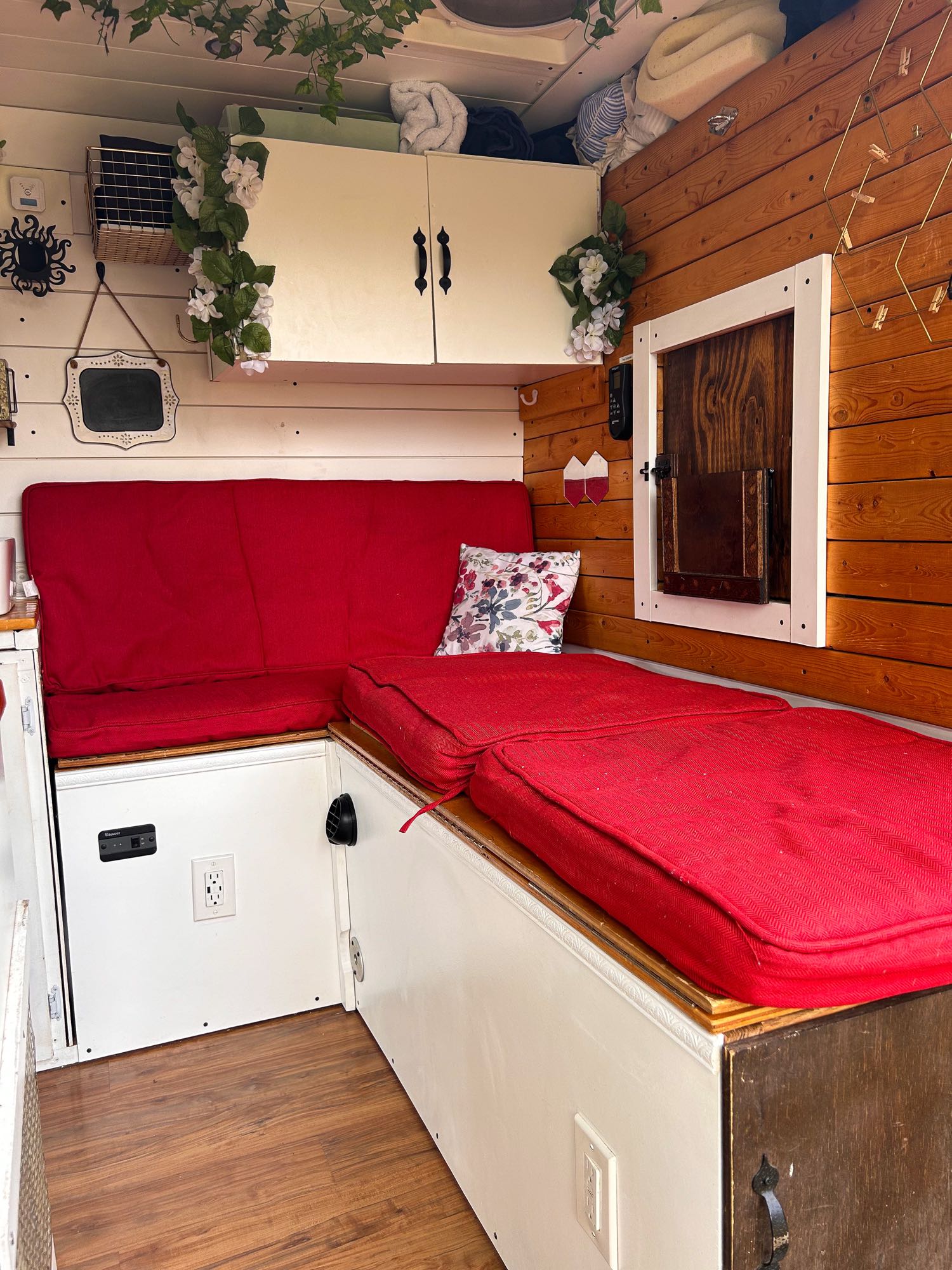 Inside a cozy RV rental: red cushioned seating/bed, wooden walls, white cabinets, & small window.. Ram Dodge Promaster 3500 2019