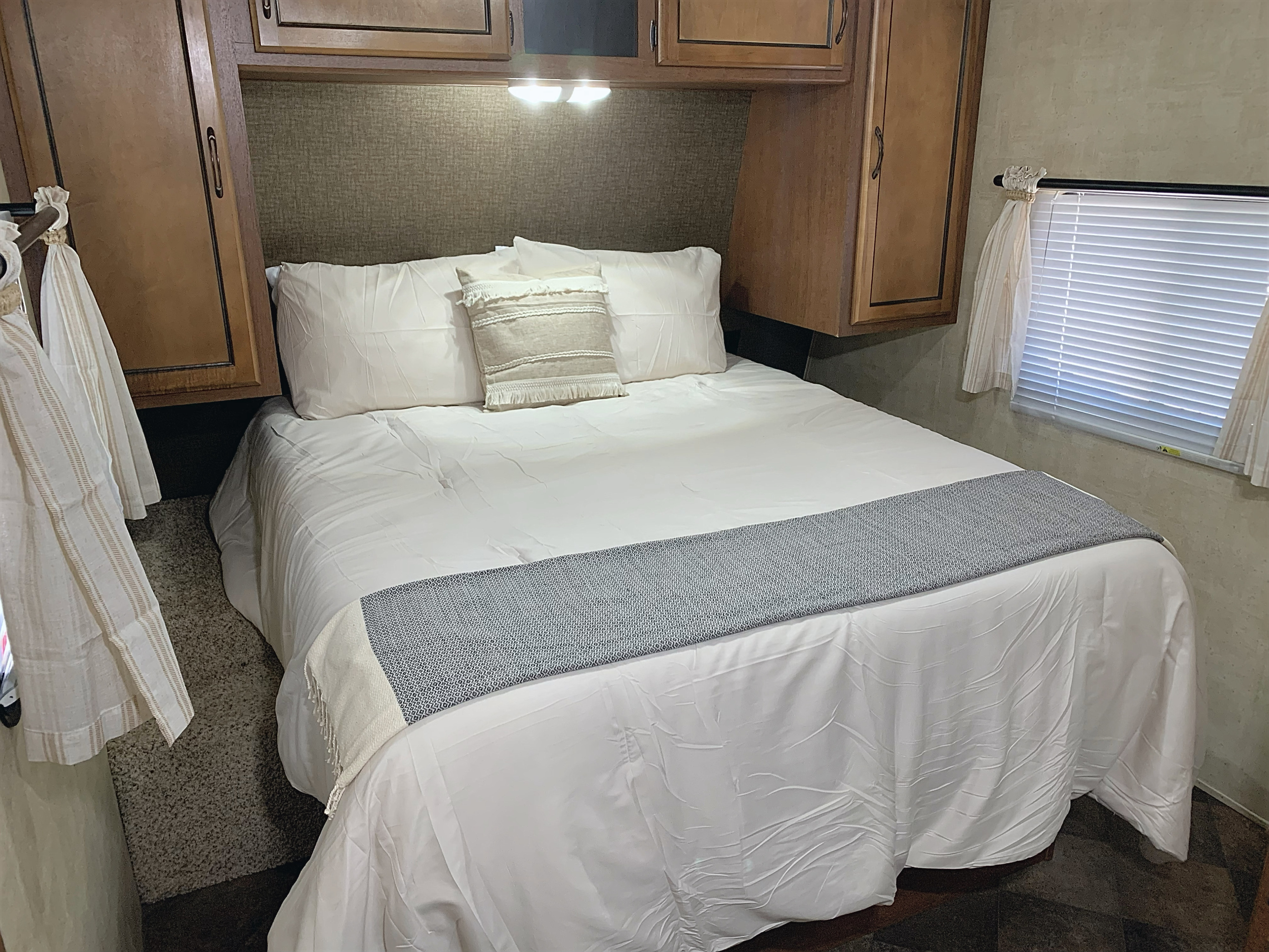 Comfortable RV rental bedroom: a made bed with white linens, overhead storage, and window.. Keystone RV Summerland 2013