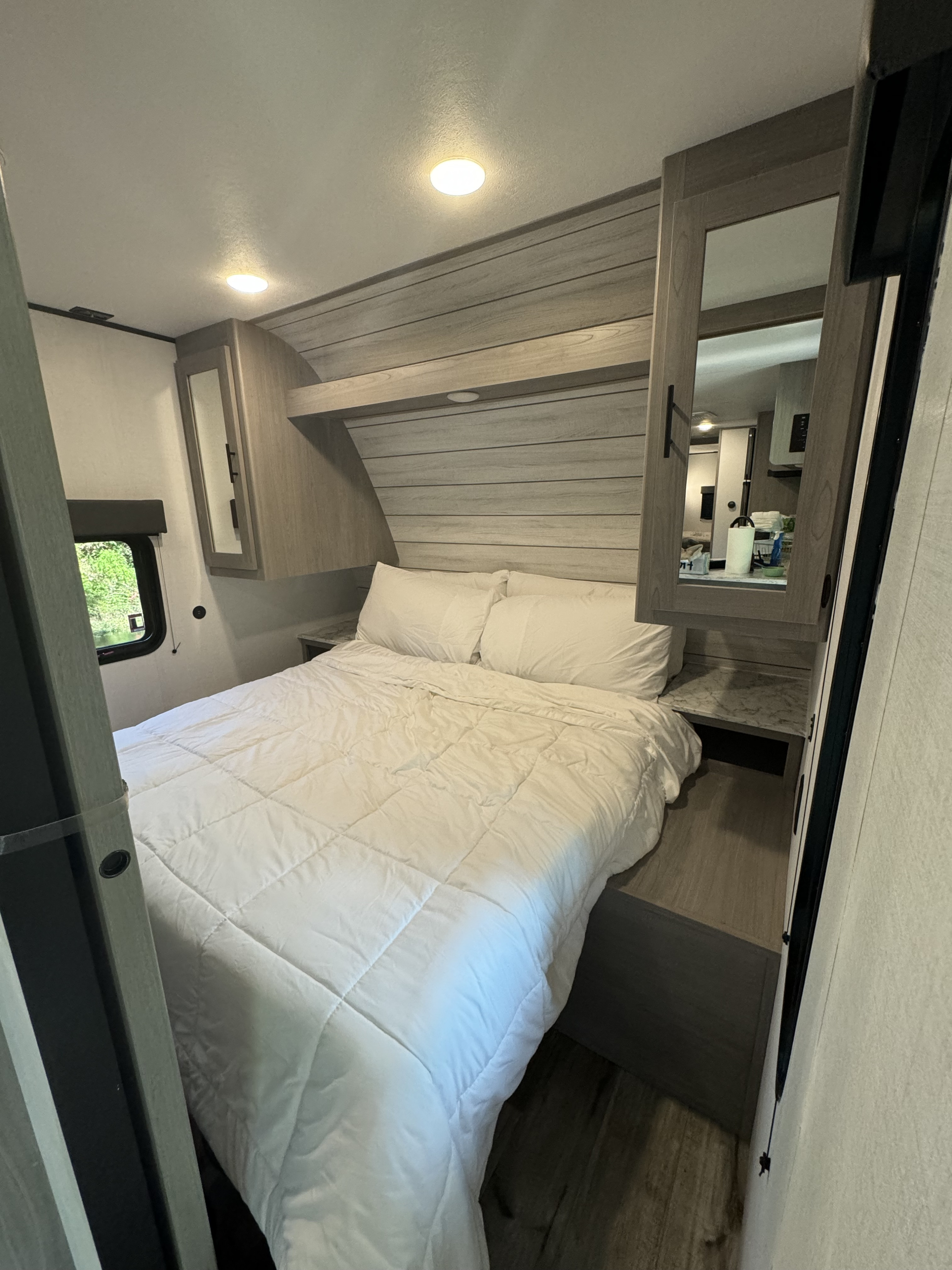 Clean, compact bedroom inside an RV rental with white bedding, overhead storage, and a window view.. Coleman Lantern 334BH 2024