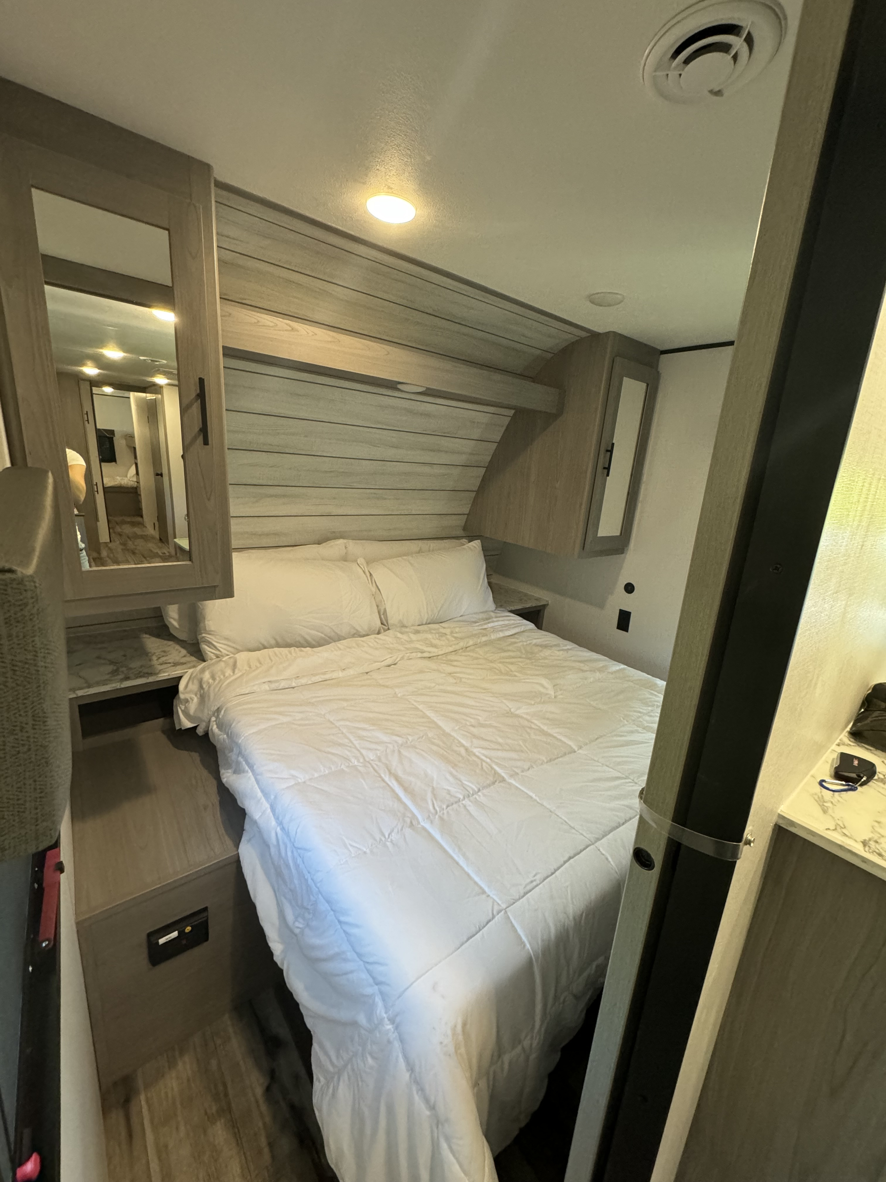 Cozy RV rental bedroom featuring a bed with white bedding, overhead cabinets, and a modern light wood interior.. Coleman Lantern 334BH 2024