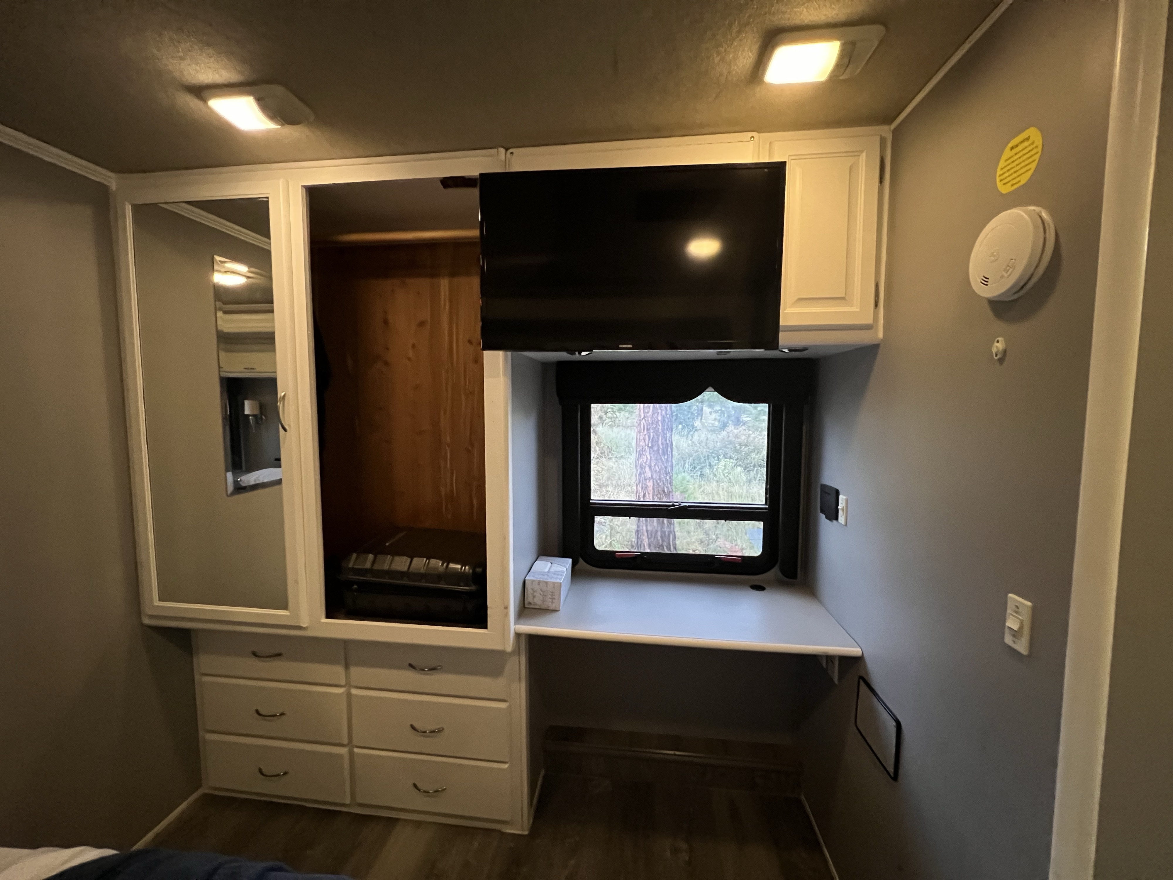Inside an RV rental: a compact bedroom setup with a mirrored wardrobe, TV, window, desk, and storage drawers.. Fleetwood Southwind 32VS 2006