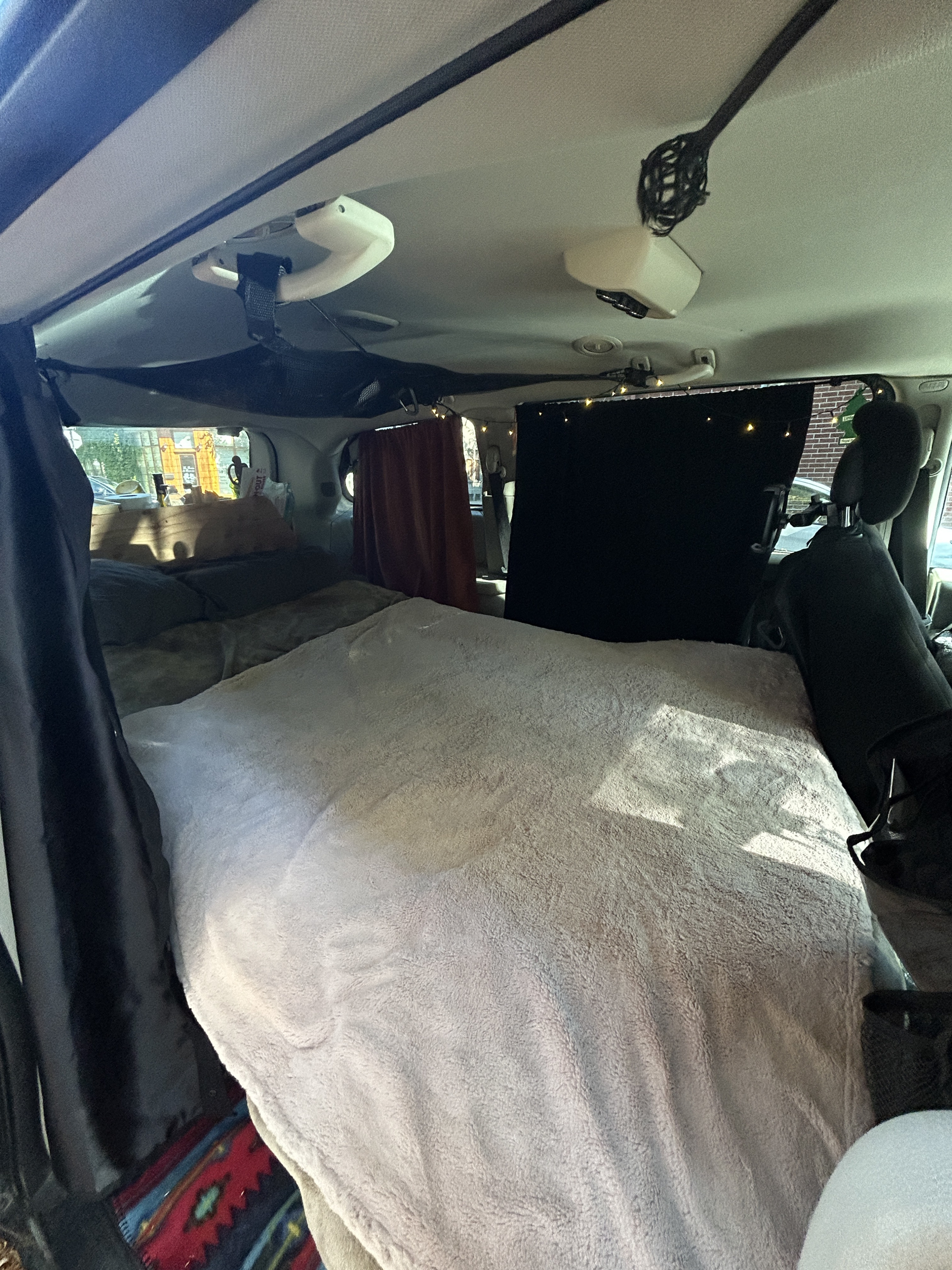 Cozy RV rental interior: a comfy bed with a light blanket, privacy curtains, & ambient string lights. Ready for travel!. Dodge Dodge Grand Caravan SXT 2011