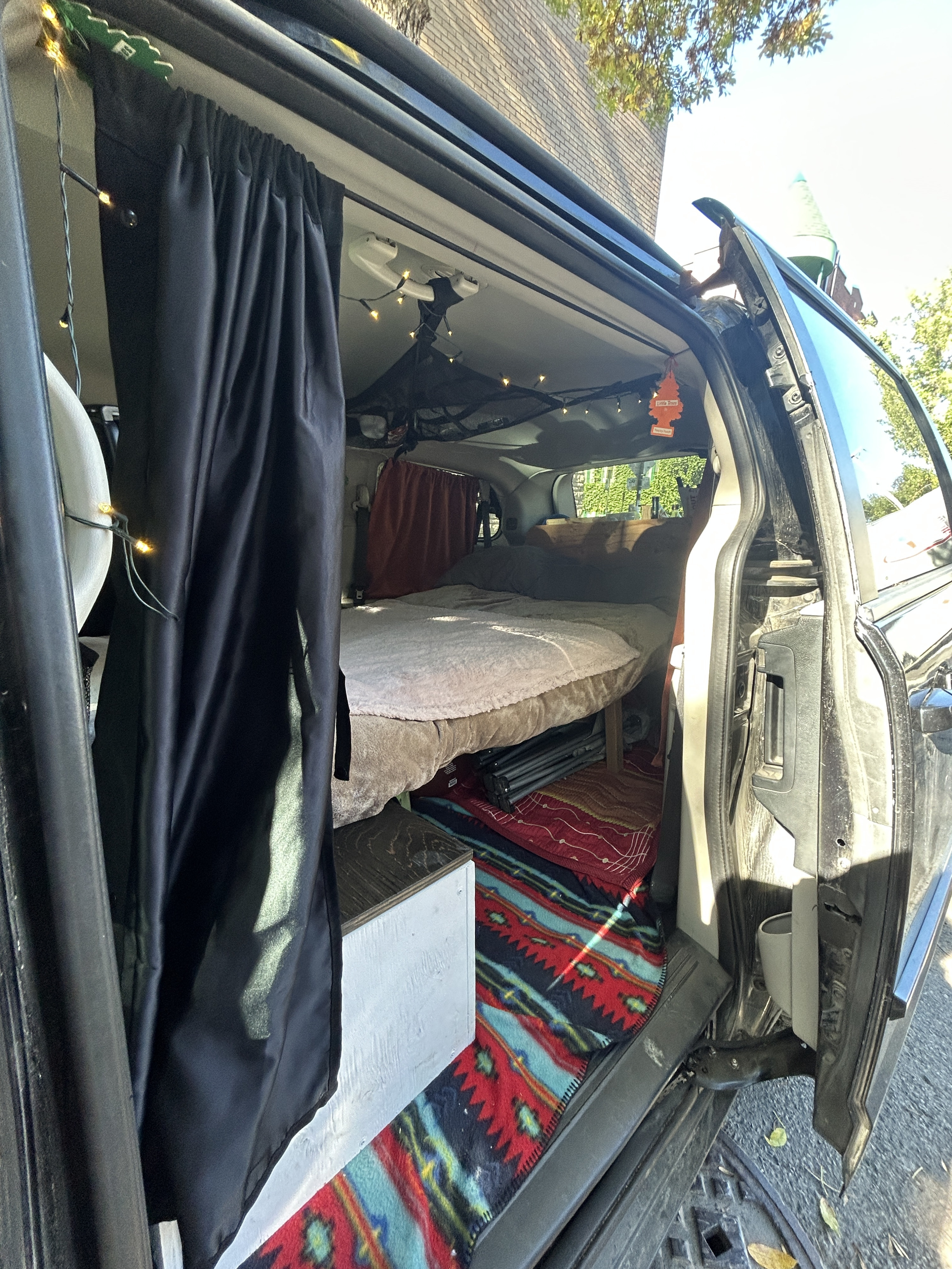 Inside a cozy camper van, ready for RV rental: a bed, privacy curtains, and string lights create a mobile home.. Dodge Dodge Grand Caravan SXT 2011