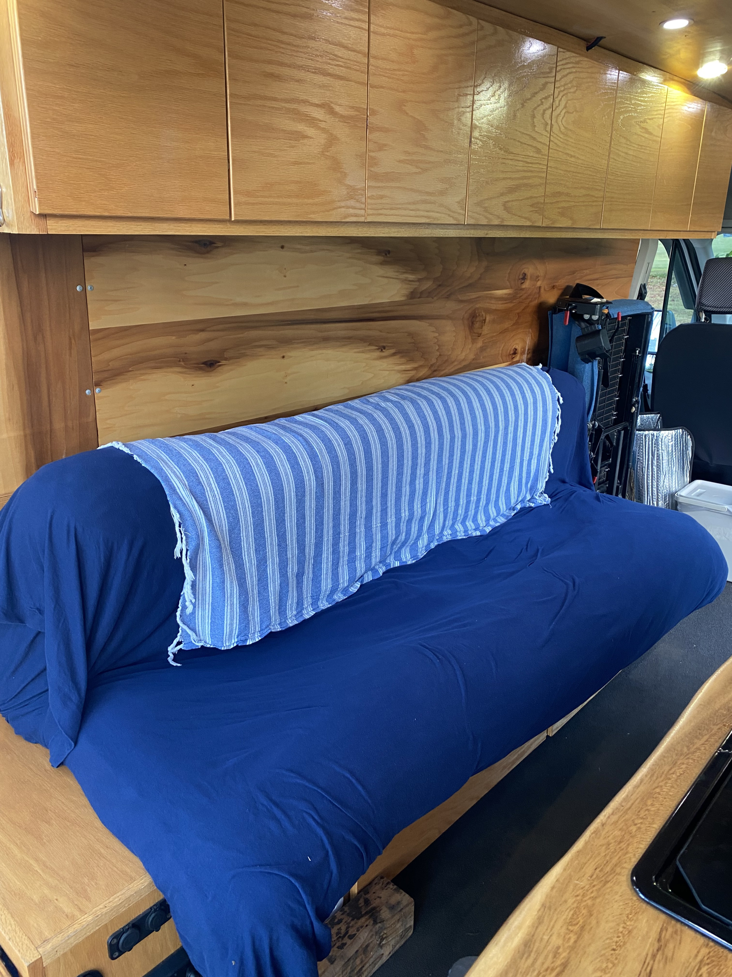 Cozy RV rental interior featuring wooden cabinets, a blue couch/bed with striped blanket, and ceiling lights.. Ford Transit 2018
