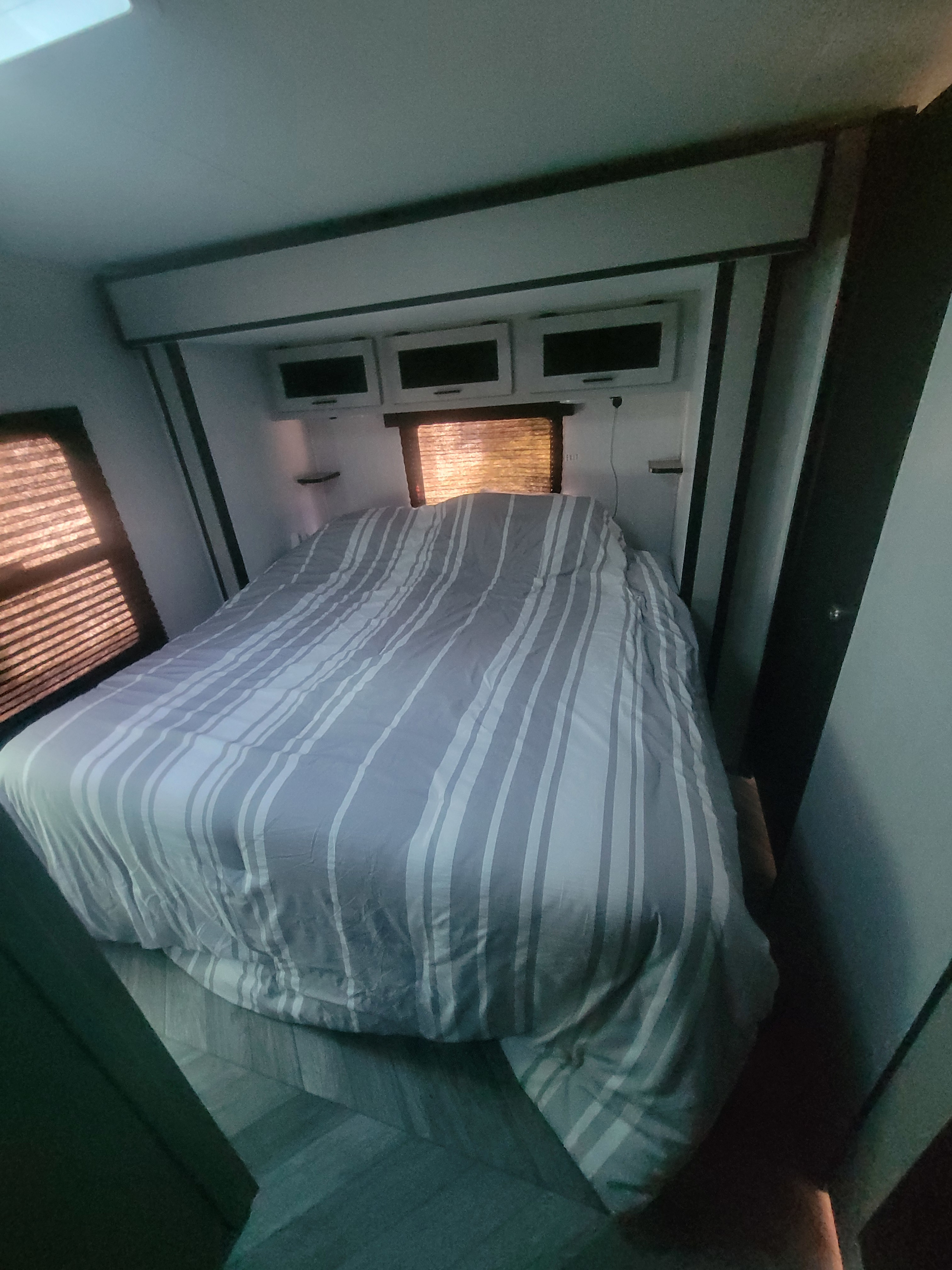 Comfortable RV rental bedroom with striped bedding, perfect for mobile adventures. Features overhead storage and window blinds.. Heartland RVs Mallard 2023