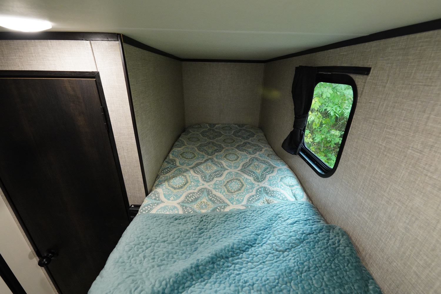 This cozy RV rental sleeping area features a bed with patterned bedding, a window with views, and a nearby door.. Jayco Jay Flight 2022
