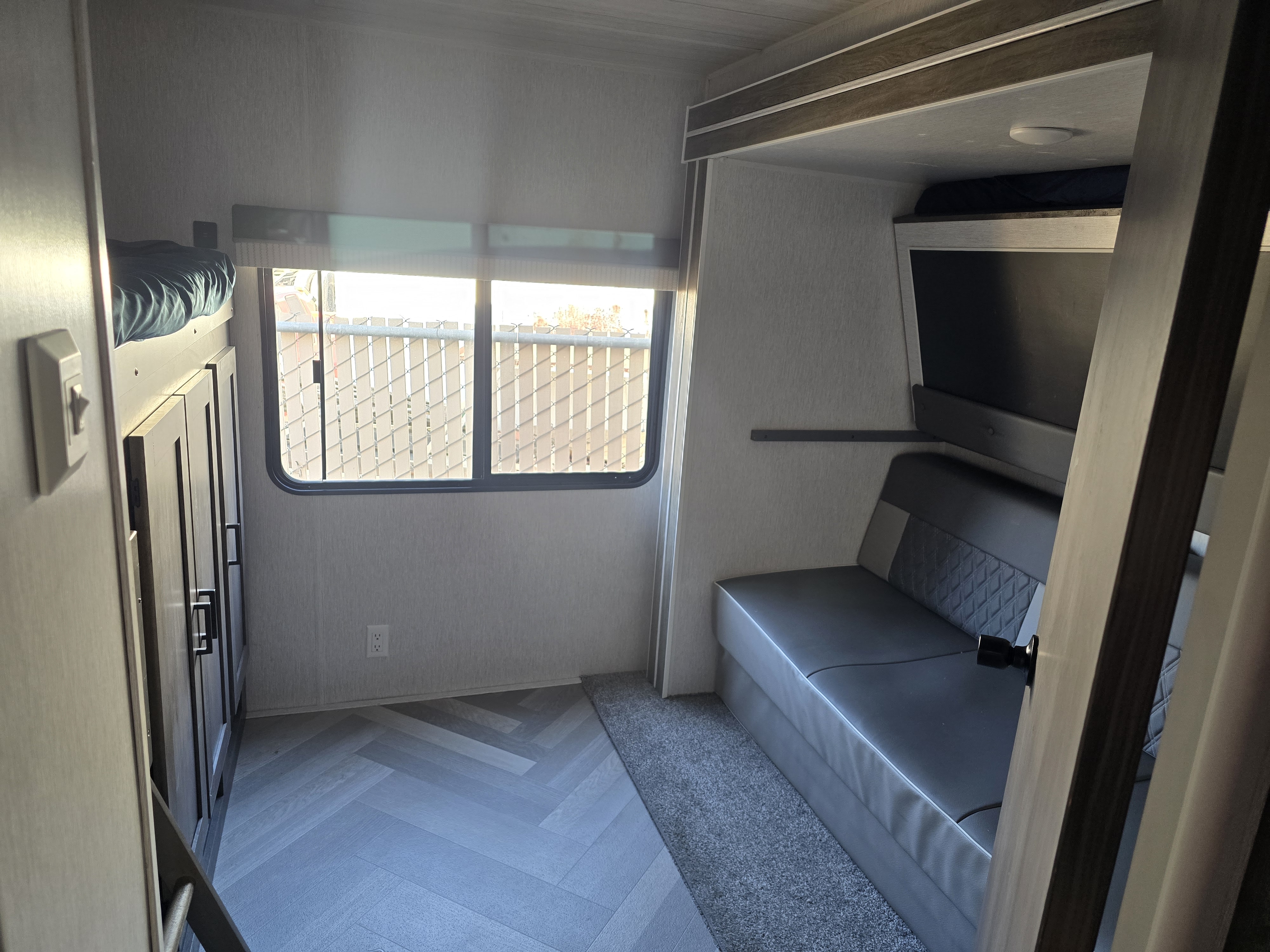 Cozy RV rental interior: bunk bed, window view of a fence, and gray sofa/dinette. Ideal for your next camper adventure.. Forest River Wildwood 2022
