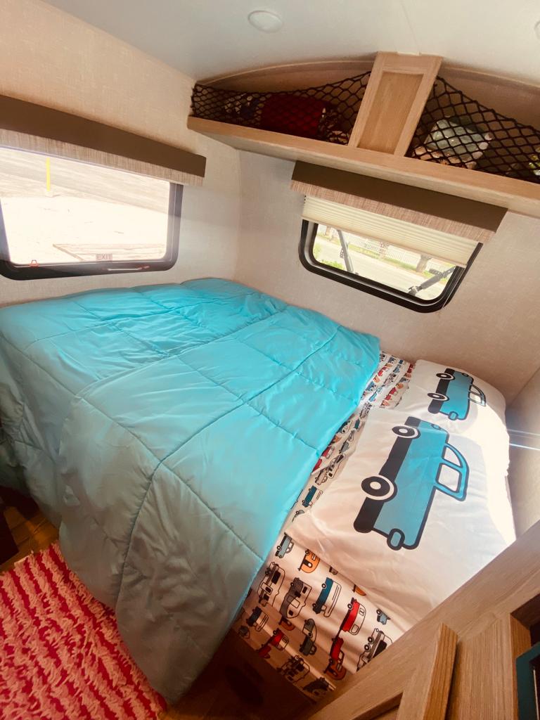 RV rental interior featuring a main bed, bunk with car sheets, windows, & netted storage. Cozy travel space.. Forest River Flagstaff E-Pro 2022