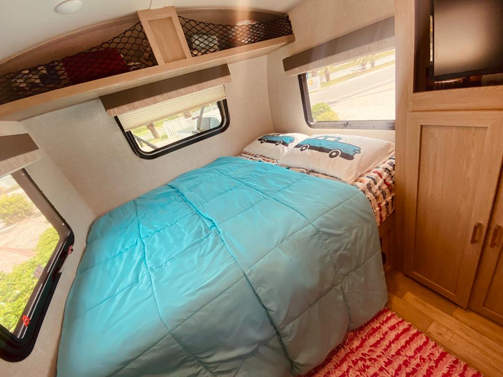 Bright RV rental bedroom features a comfy bed with car pillows, windows, and overhead storage, ideal for travel.. Forest River Flagstaff E-Pro 2022
