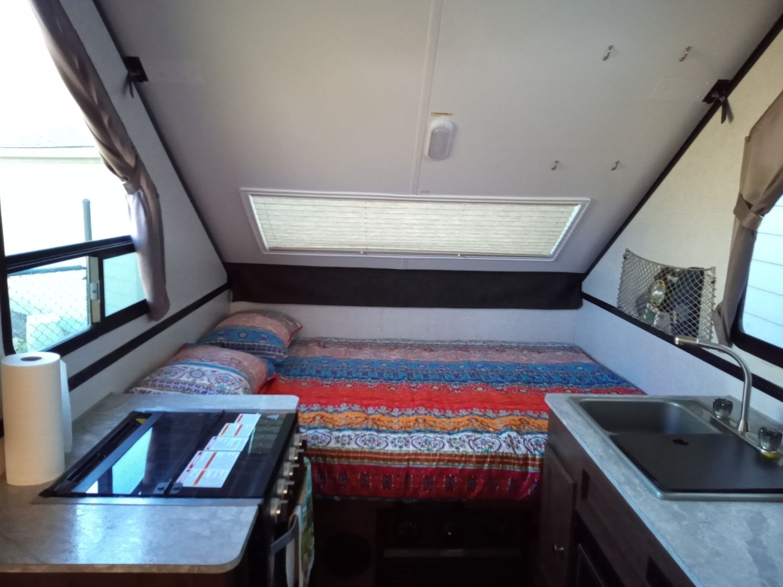View inside a compact **rv rental**: a colorful bed fills the back, with a small kitchen (stove, sink) in the foreground.. Forest River Flagstaff Classic 2021
