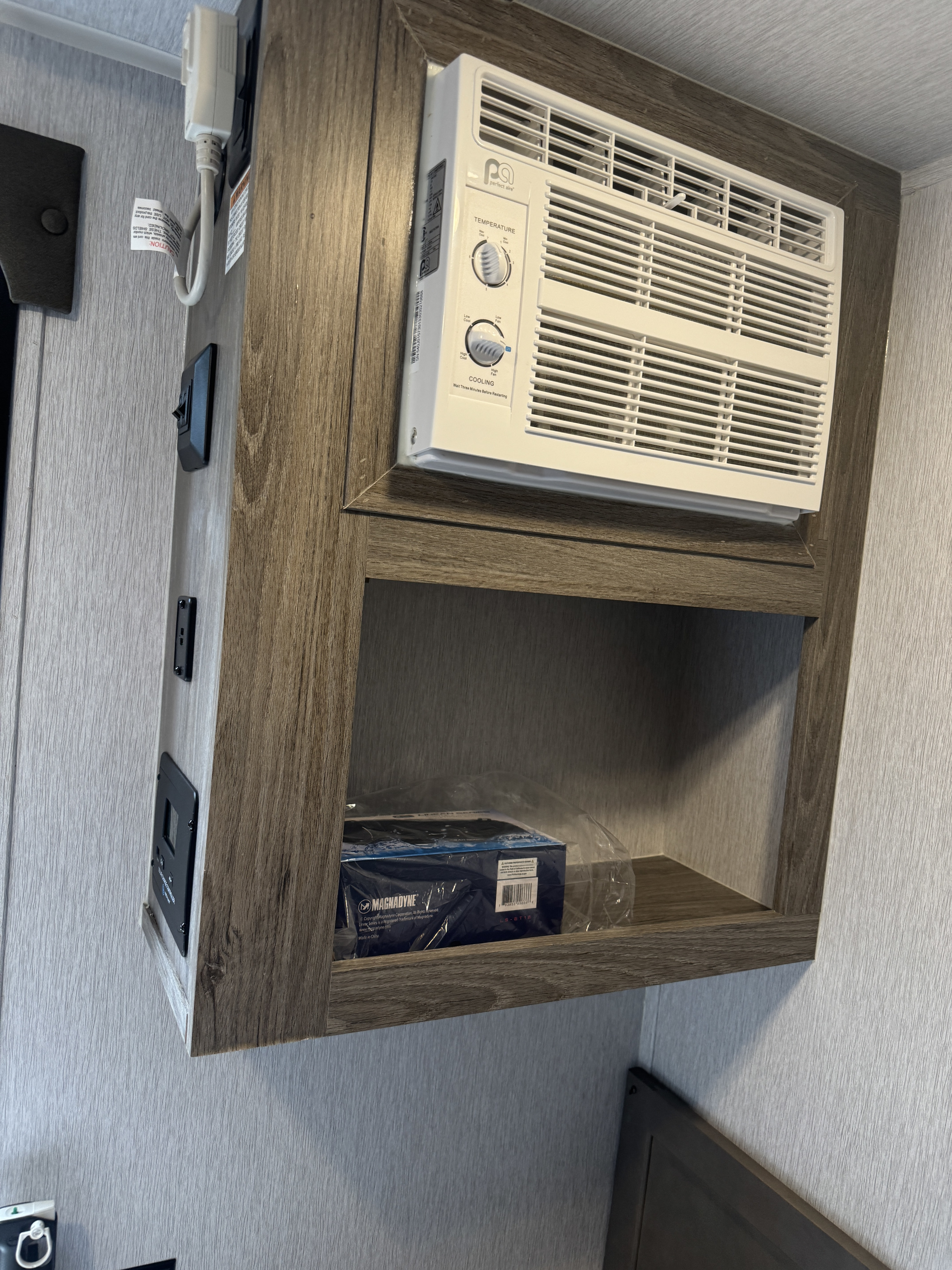 RV rental: Compact Perfect Aire AC unit and storage shelf with electronics, highlighting efficient use of space in this RV interior.. Sunset Park RV SunRay 2024