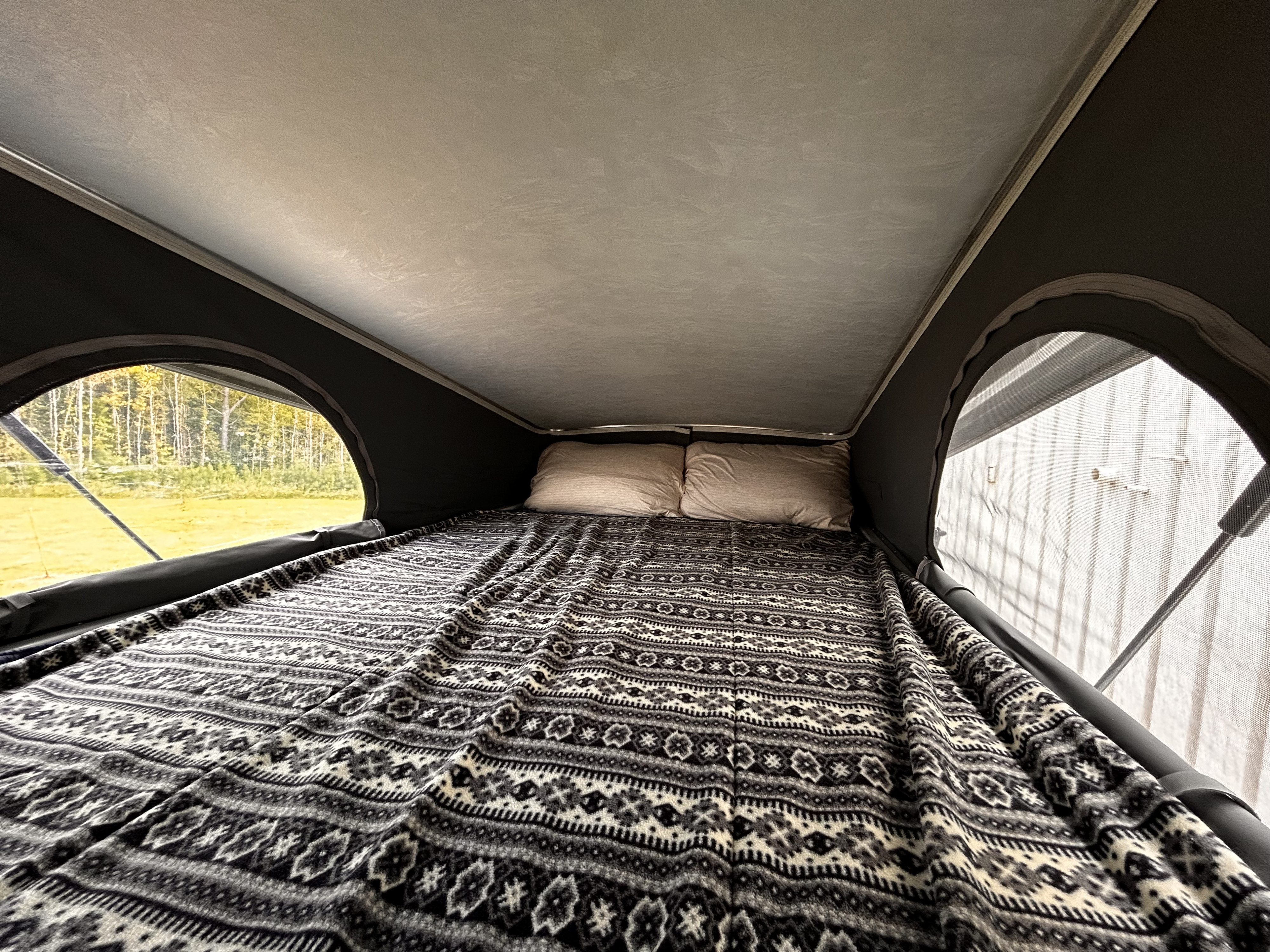 Experience comfort in this RV rental! A pop-top camper bed with a patterned blanket, pillows, and views of nature.. Winnebago Solis 2021