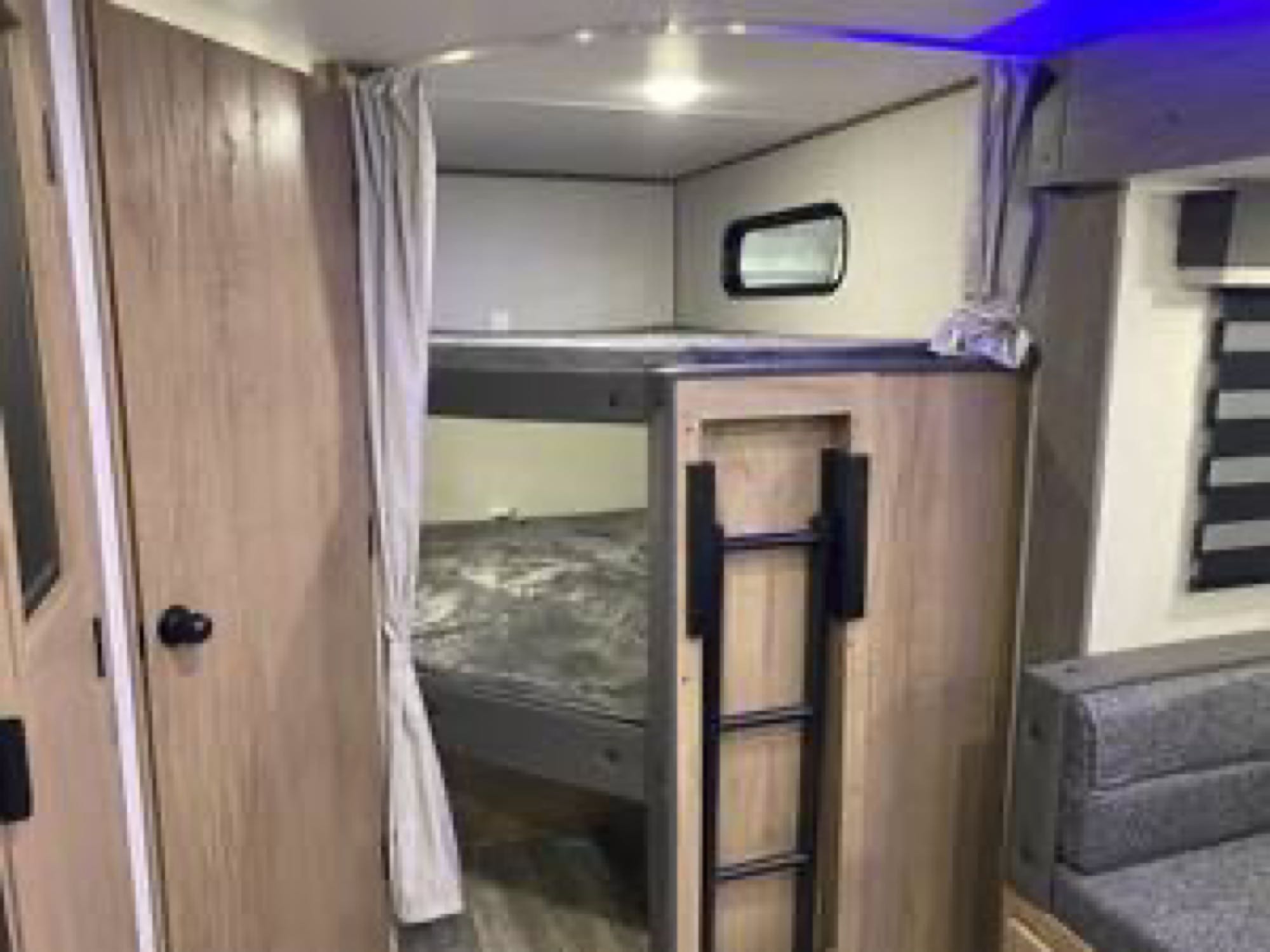 RV rental interior: A wooden-paneled space with stacked bunk beds, a ladder, window, and a gray sofa for comfortable travel.. Forest River Alpha wolf 26 Dbh-l 2024