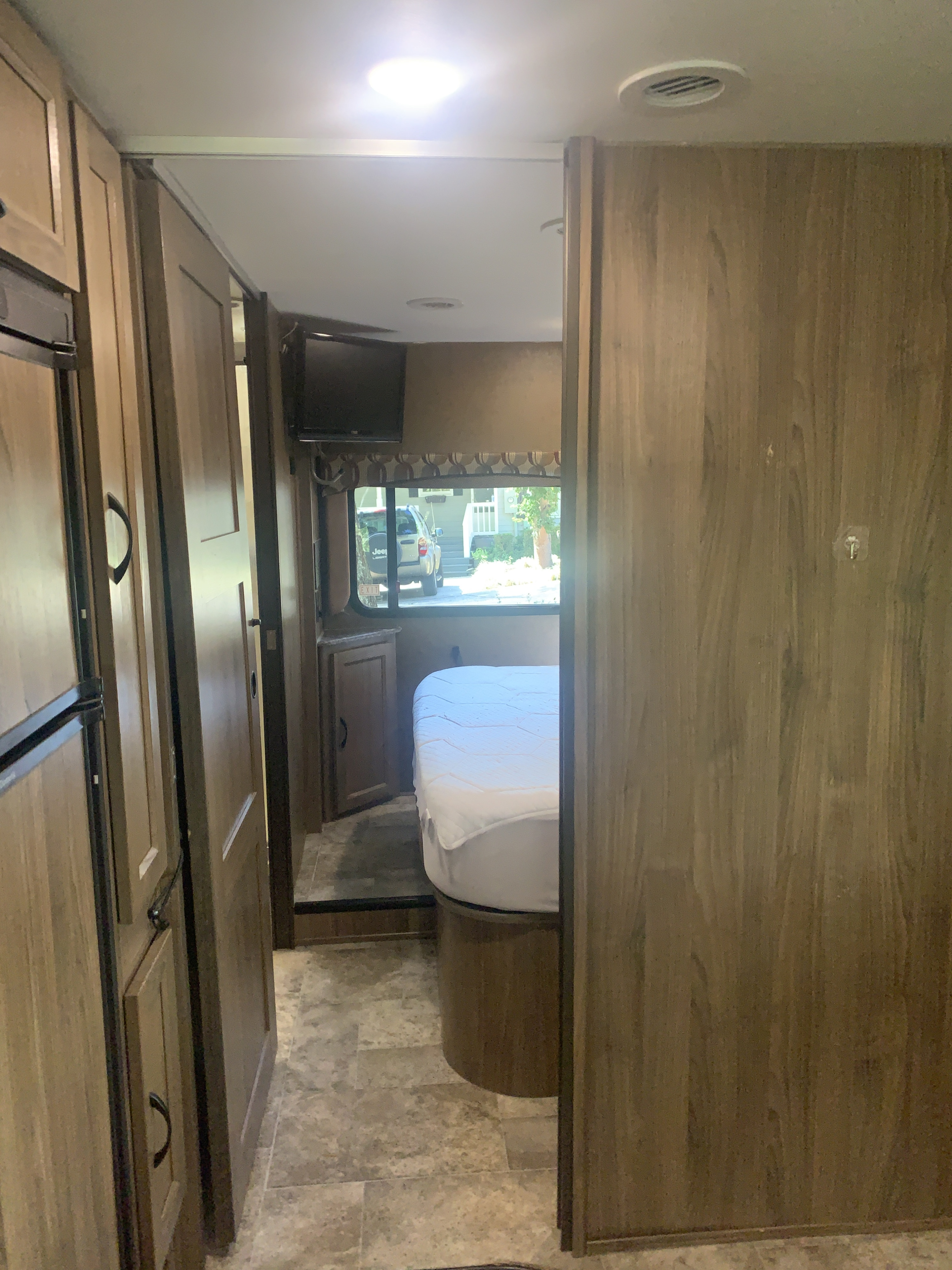 Interior of an RV rental showing a hallway leading to a bedroom with a bed, and wood-toned cabinetry.. Forest River Coachmen Freelander 2017