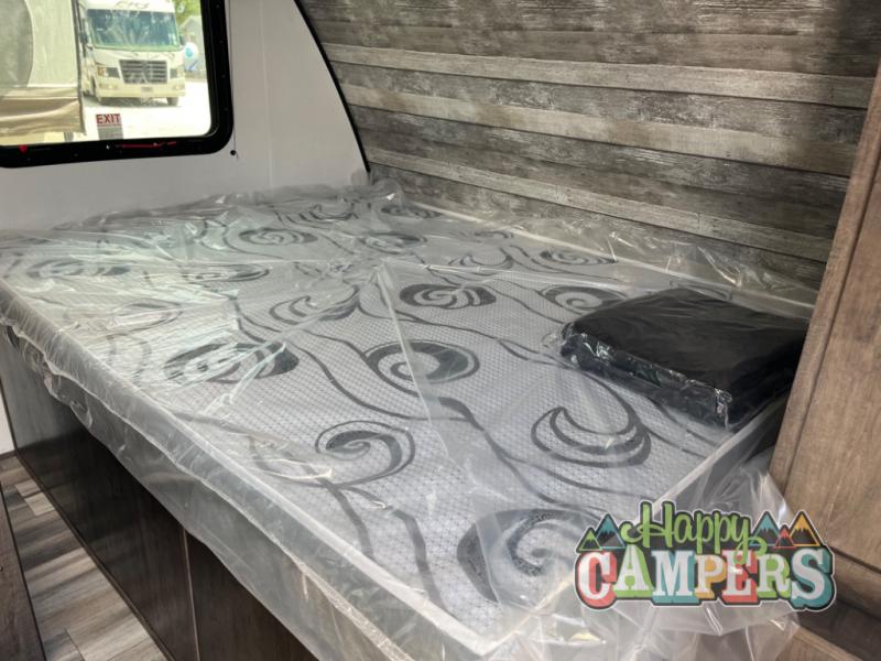 New RV rental bed with mattress and folded item, both in protective plastic. An "EXIT" sign is visible through the window.. Riverside Rv Intrepid 190BHi 2023