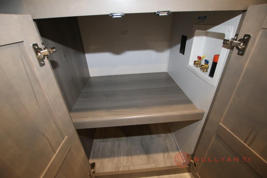 RV rental interior: A cabinet with a shelf and visible washer/dryer hookups (red/blue valves) for utility.. Keystone RV Montana 2023