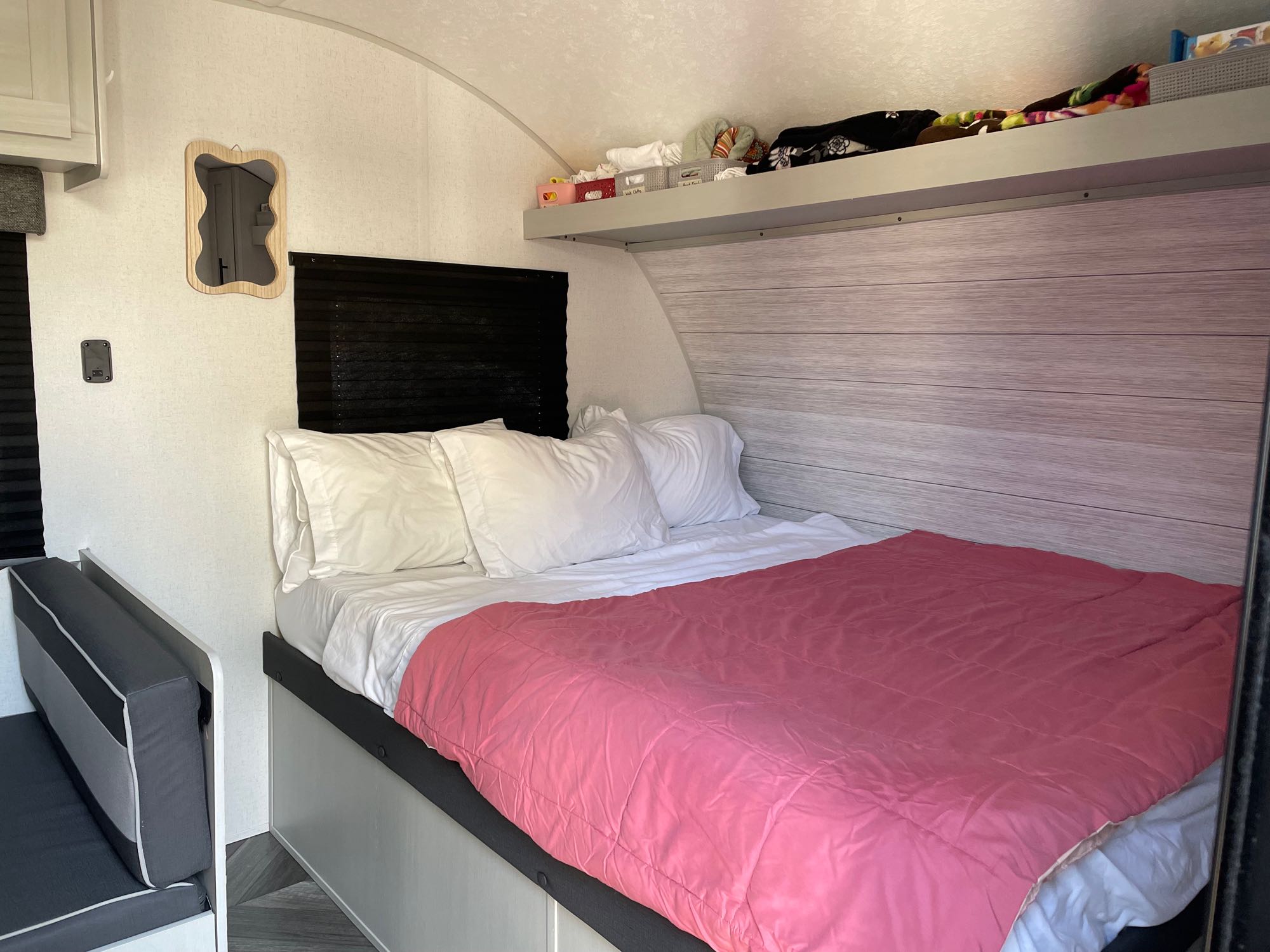 Inside an RV rental: a bright bedroom with a bed, white linens, pink comforter, and overhead storage.. Forest River Salem FSX Plantium 2022