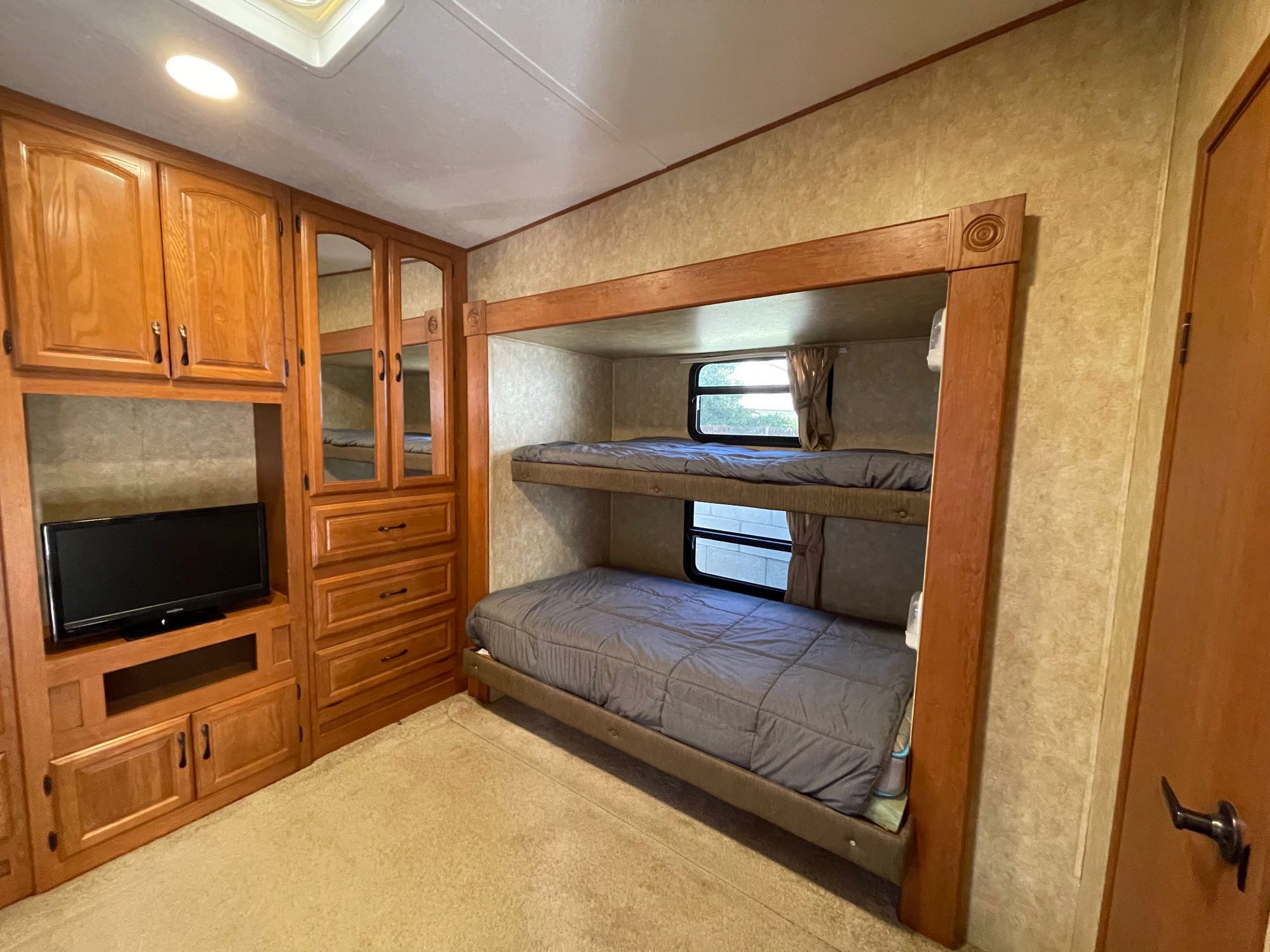 RV rental bedroom featuring comfortable bunk beds, built-in TV, and ample wood storage.. Forest River Sandpiper 2011