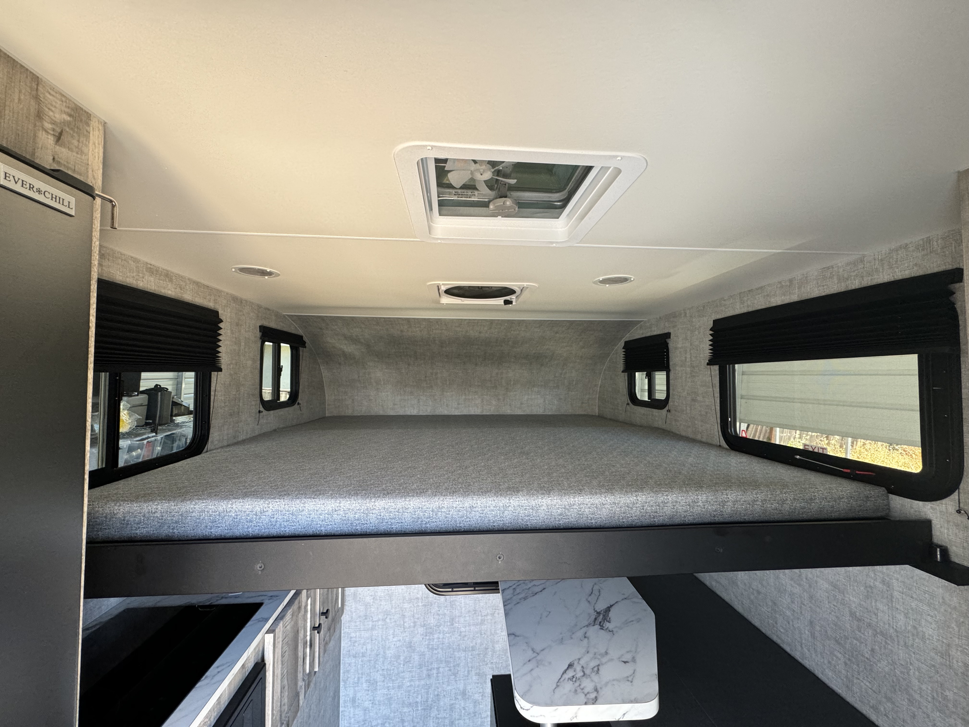 Modern RV rental interior: large overhead bunk, side windows with blinds, and "EVER*CHILL" fridge visible.. ADLAR 6.5XLS Truck Camper ADLAR 6.5XLS Truck Camper 2024