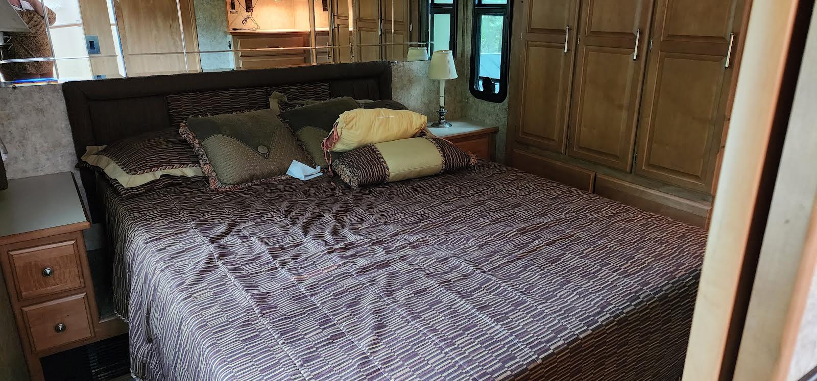 Cozy RV rental bedroom with a large bed, nightstand, and built-in cabinets. Mirrored headboard adds to the spacious feel.. Winnebago Journey 2006