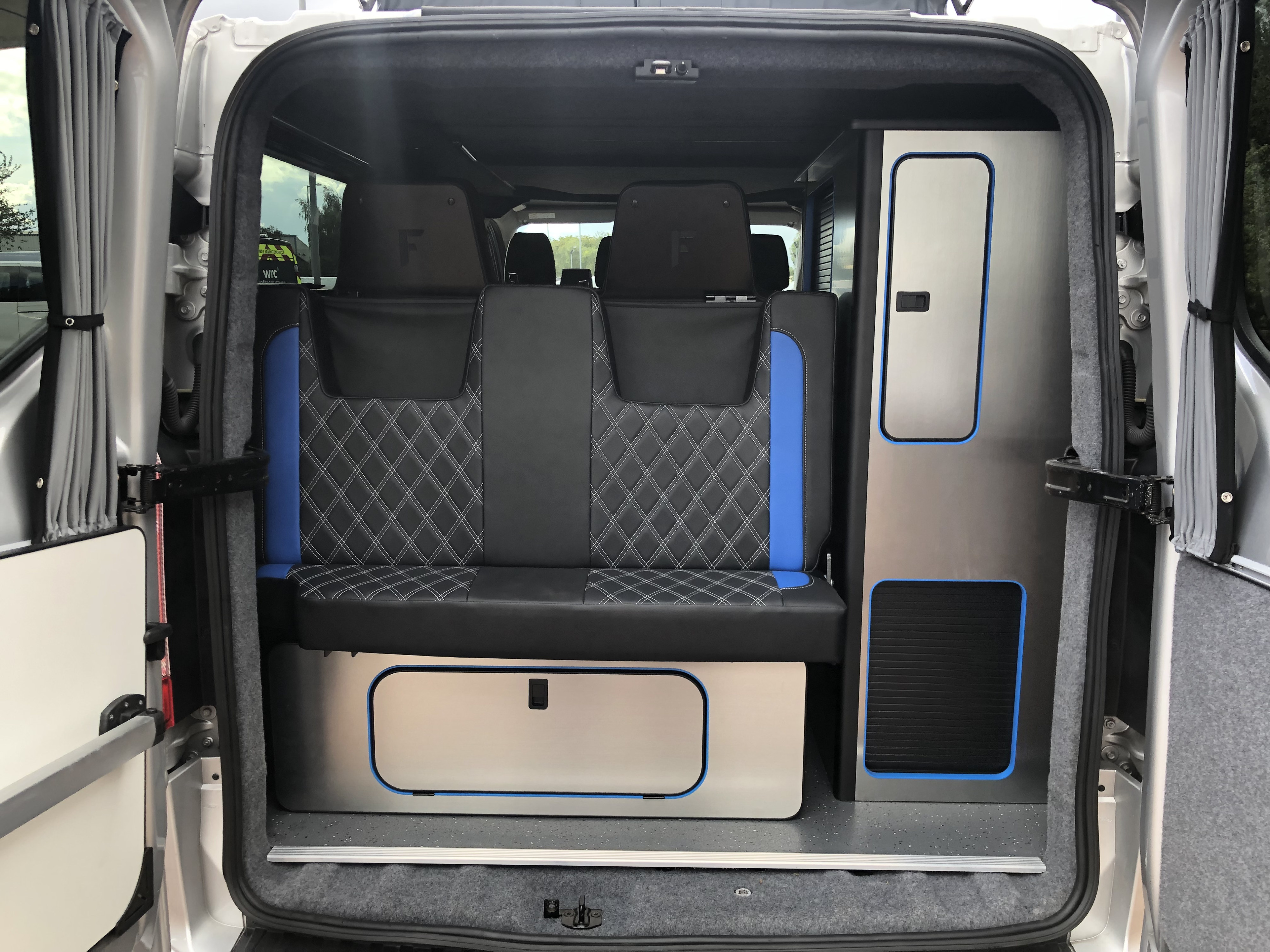 Explore this RV rental's modern camper van interior, featuring a blue and black diamond-stitched bench seat and custom storage cabinetry.. Ford Transit Custom 2.0 TDCI 2017
