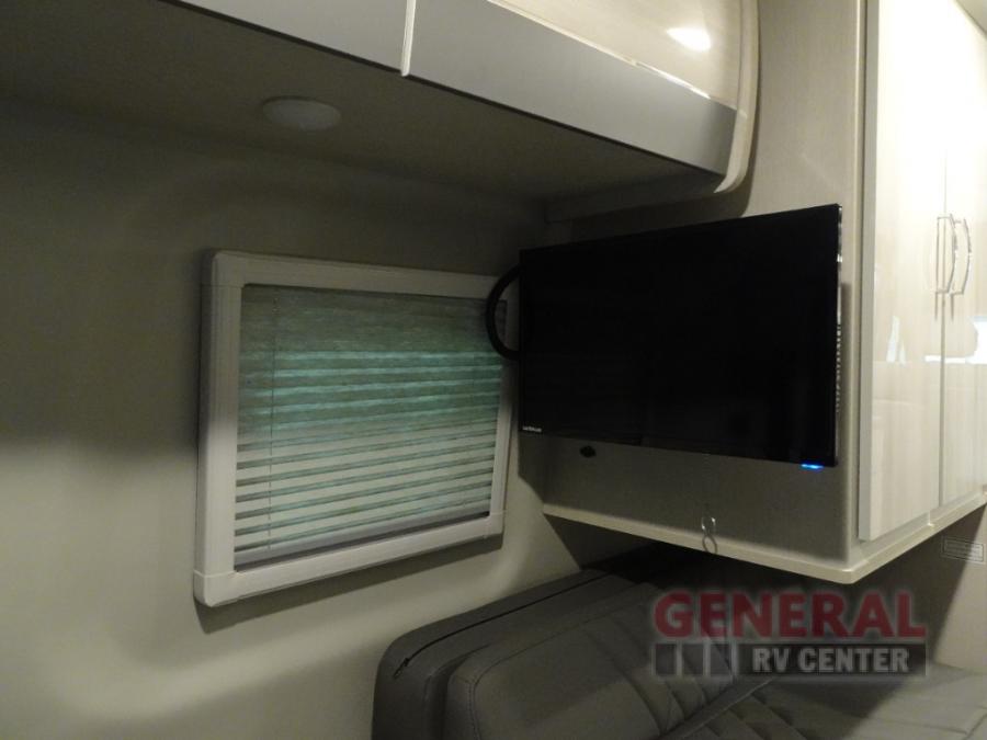RV rental bedroom: wall-mounted TV, window with blinds, and overhead storage cabinets for compact living.. Thor Sanctuary 2024