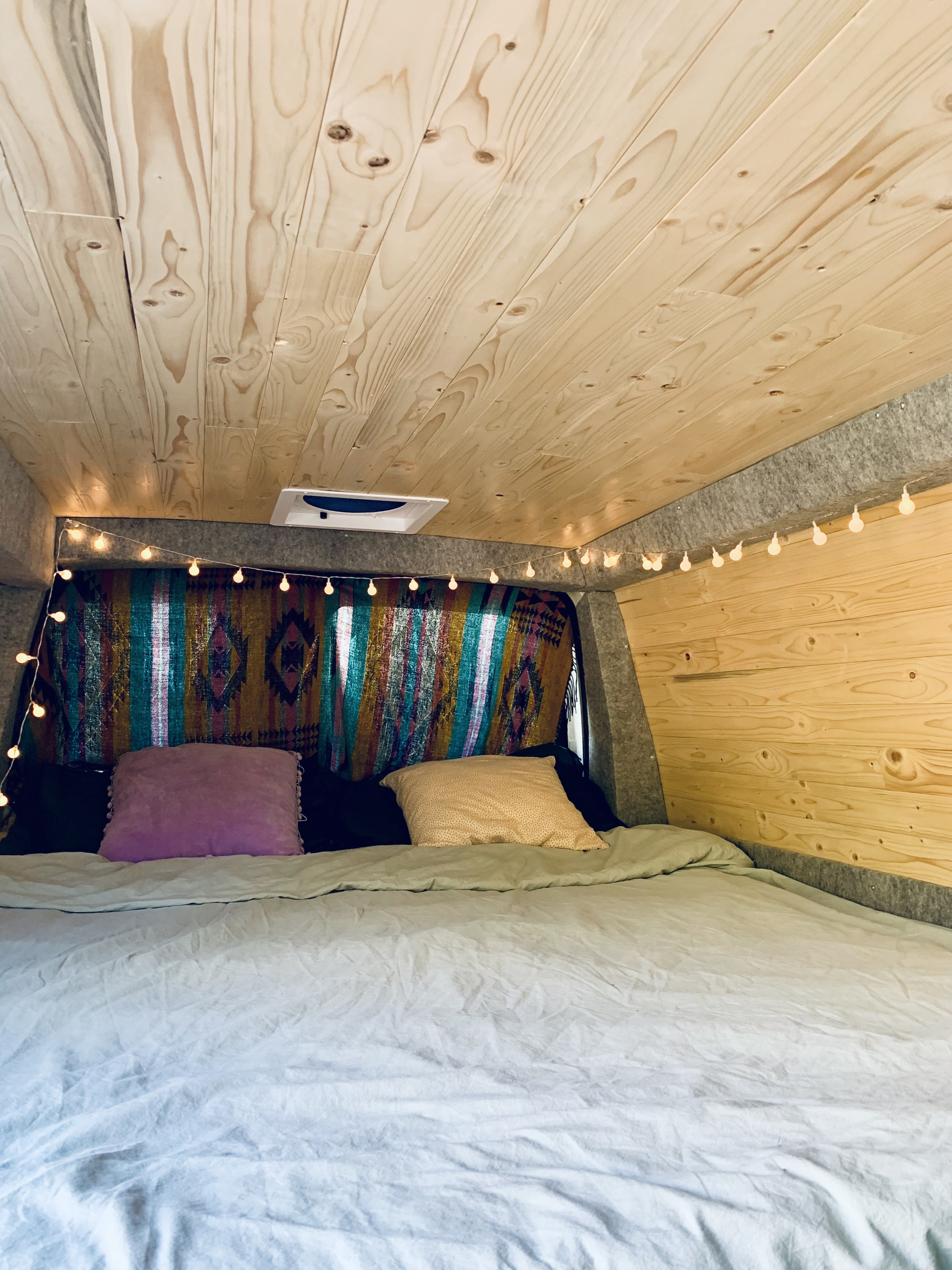 Cozy RV rental interior with wooden ceiling, string lights, and a colorful blanket over a comfy bed.. Gmc Savanna 2016