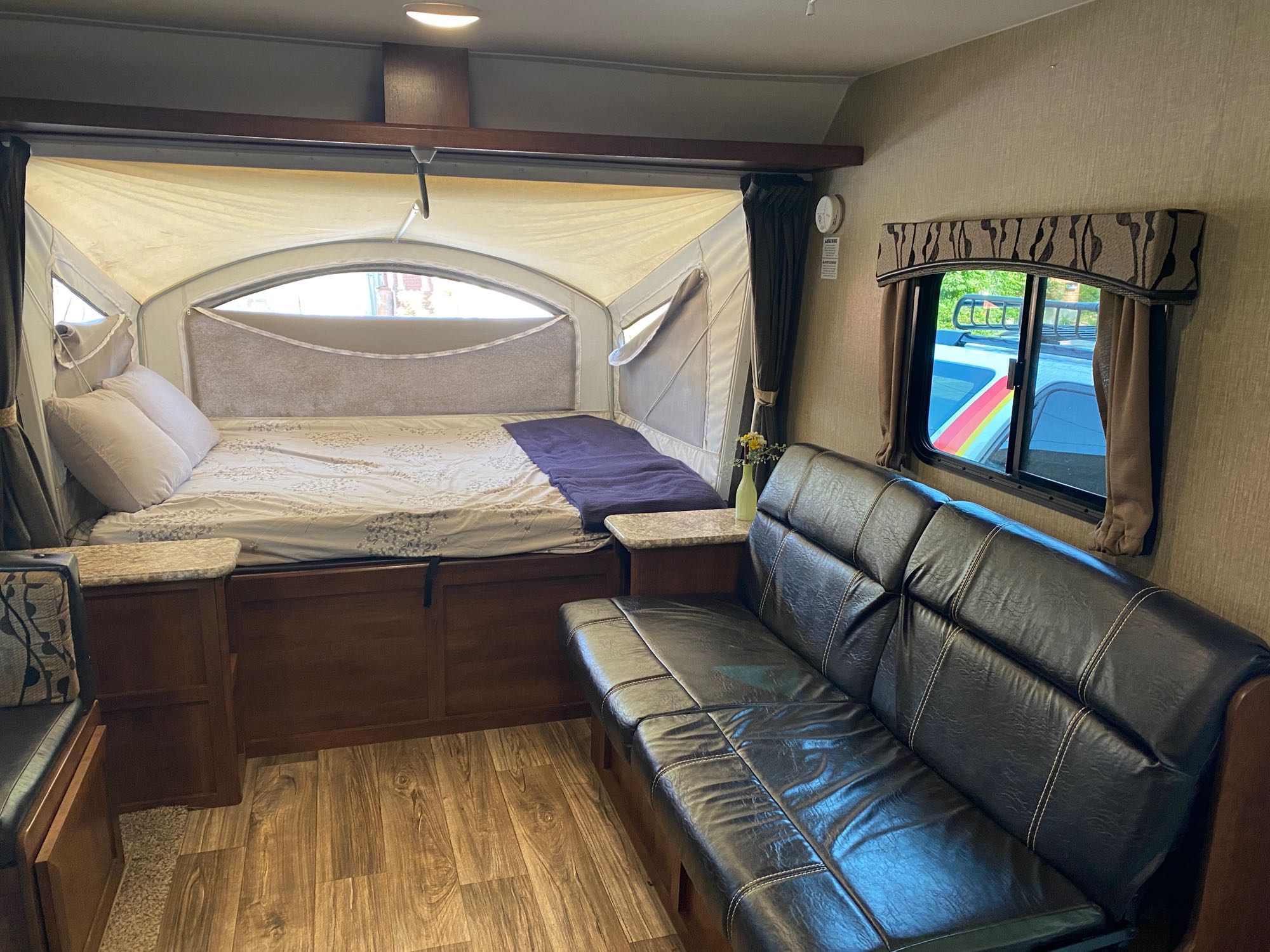 Spacious RV rental interior: an extendable bed with light bedding, dark leather sofa, and wood floors for comfy travel.. Keystone RV Passport Express 2016
