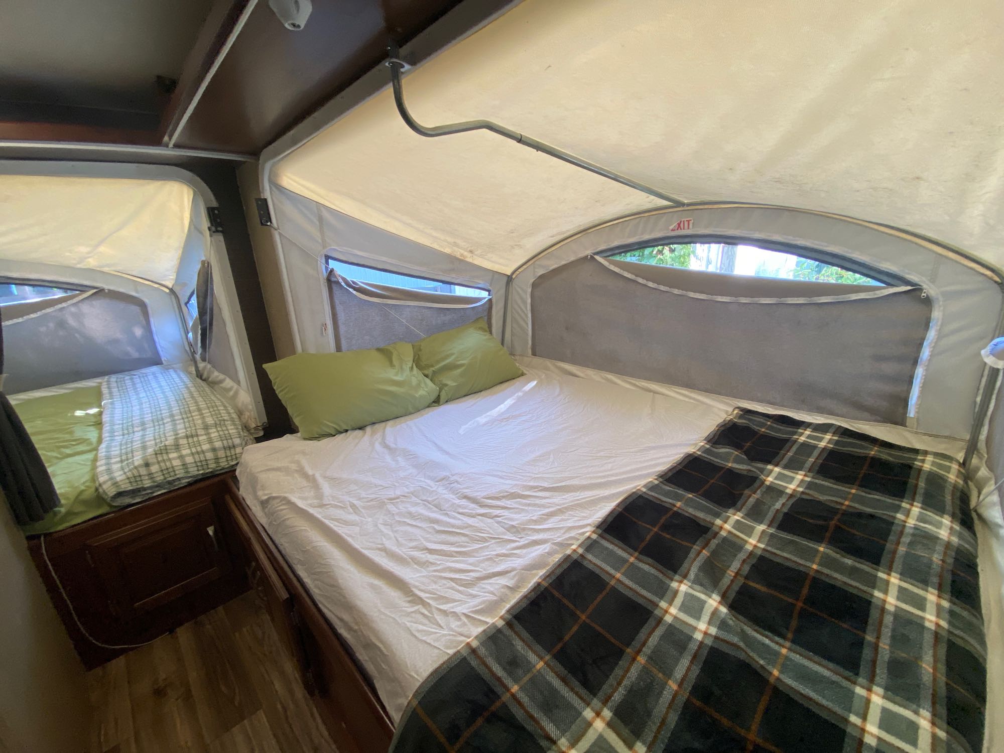 Inside a pop-up RV rental: a spacious bed with green pillows and plaid blanket, and a second bed area, ideal for camping comfort.. Keystone RV Passport Express 2016