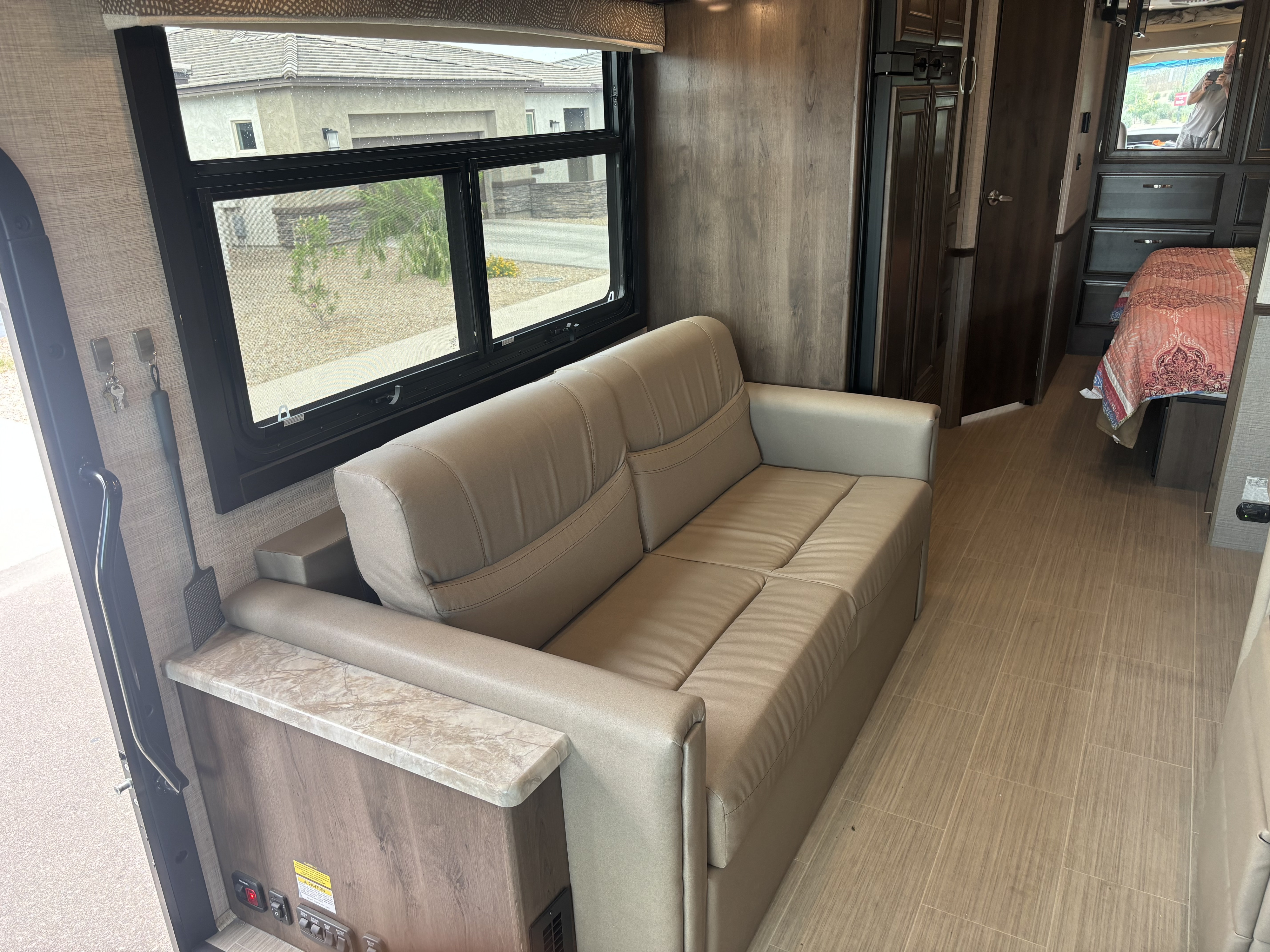 RV rental interior featuring a modern sofa, large window with outdoor view, and cozy bedroom area.. Entegra Coach Vision 2021
