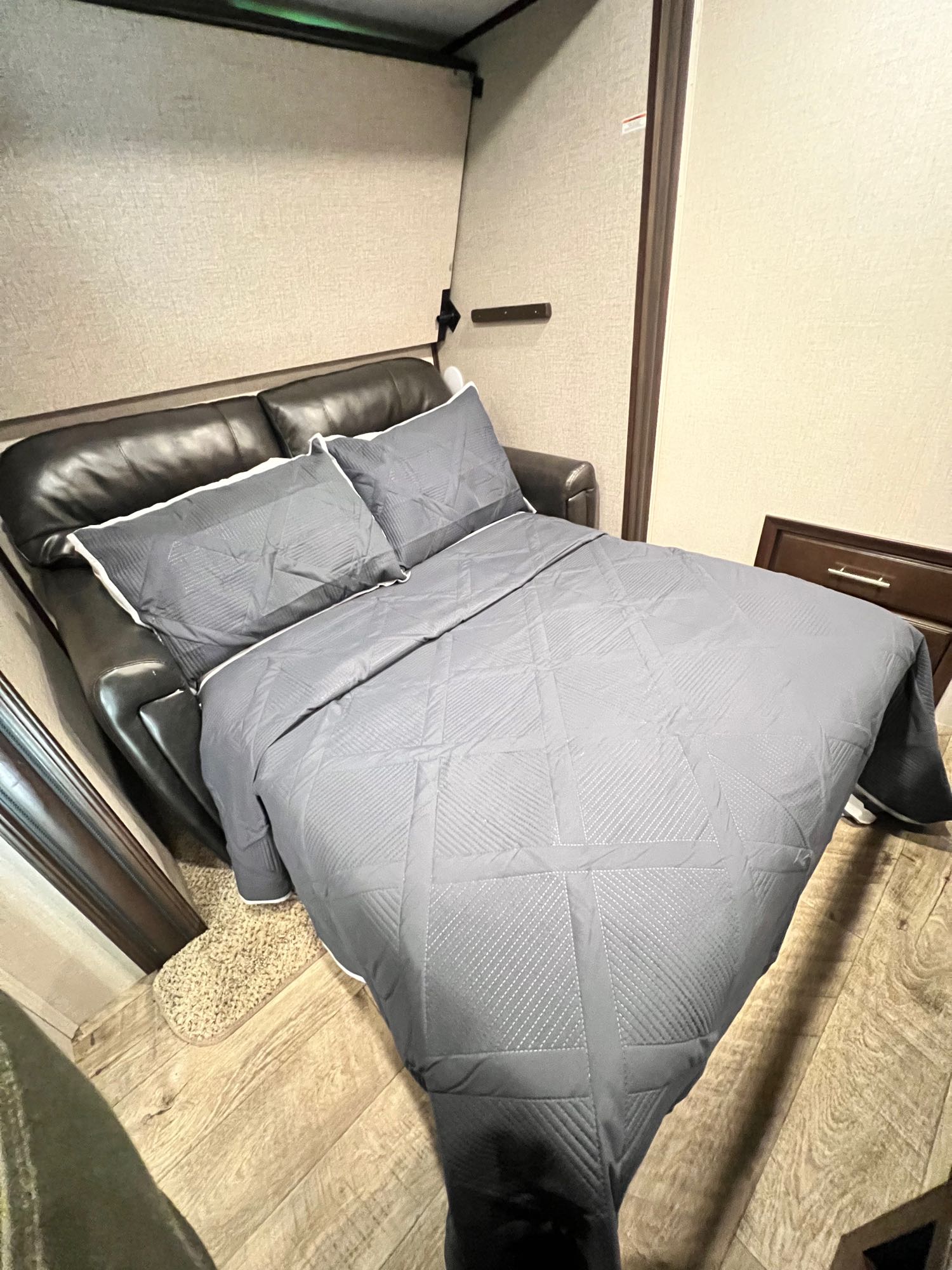 Dark leather sofa converted to a bed with gray pillows and comforter in an RV rental, offering a cozy sleeping setup.. Jayco North Point 2019