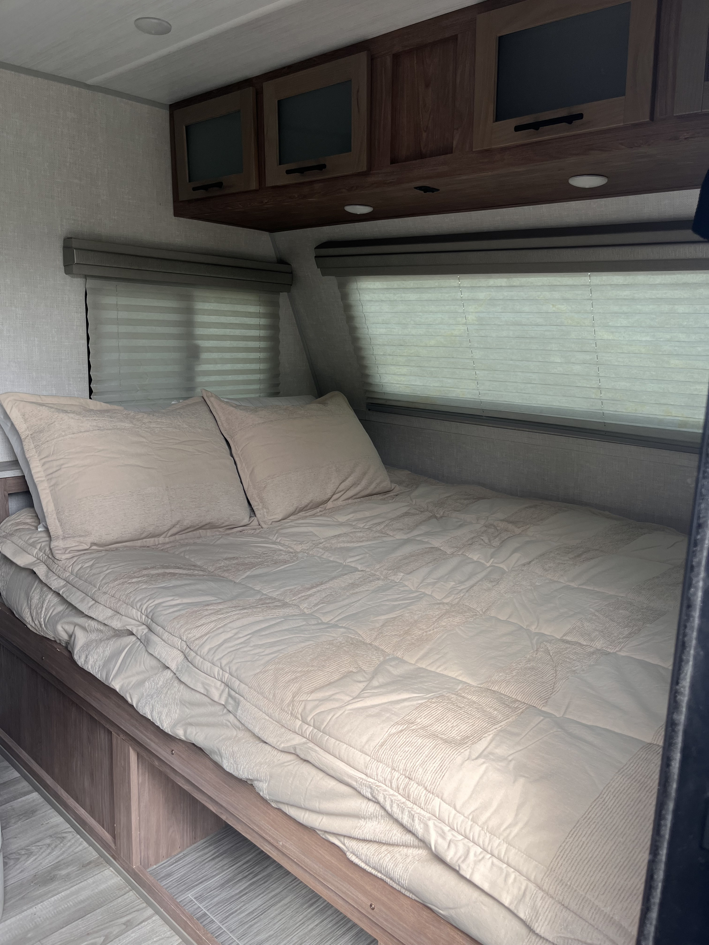 Comfortable RV rental bedroom featuring a neatly made bed with light bedding, overhead cabinets, and privacy blinds.. Forest River No Boundaries ( NO BO ) 19.8 2022