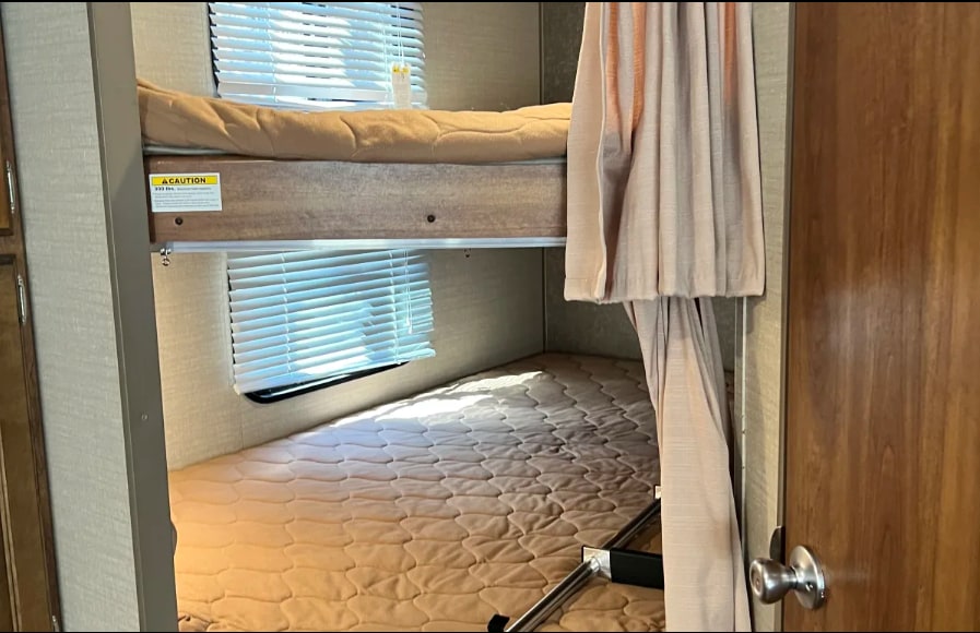 Interior of an RV rental showing cozy bunk beds, upper and lower, with windows and privacy curtains.. Keystone Springdale 2016