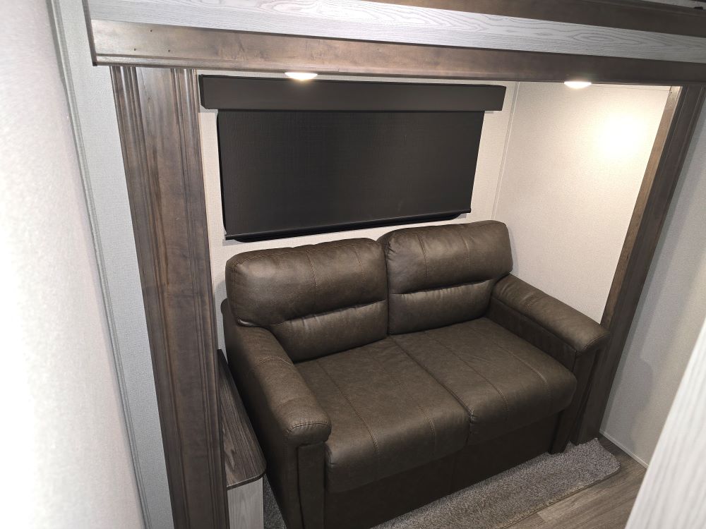 Compact brown two-seater sofa/sleeper in an RV rental's cozy nook, featuring a window with blind & overhead lights.. Keystone RV Montana High Country 2020