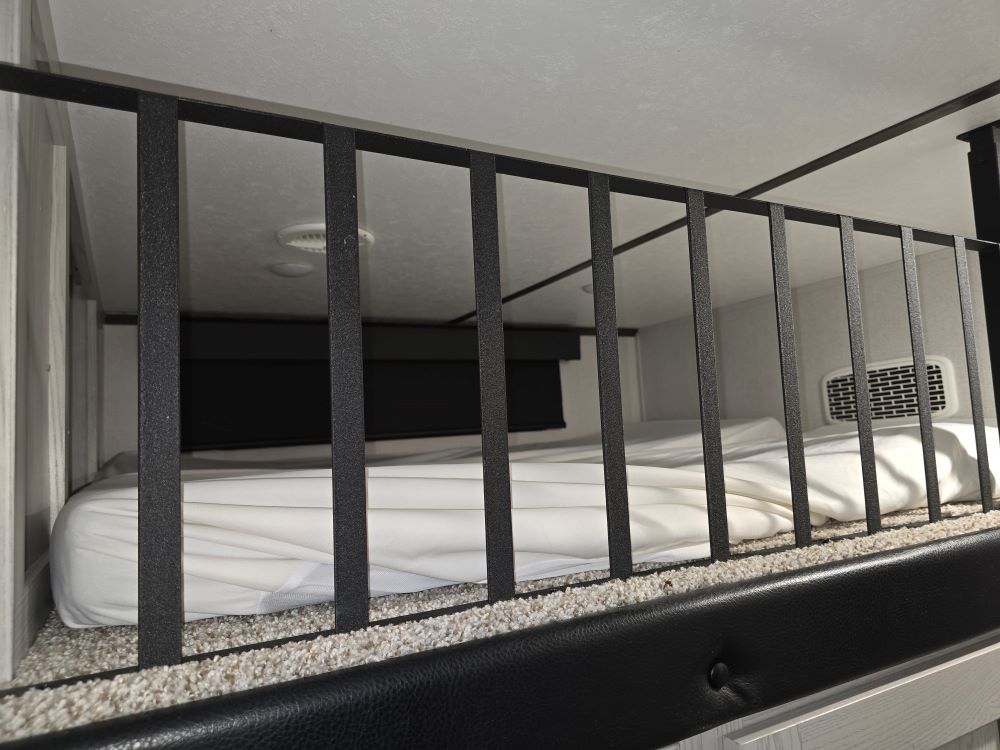 Cozy RV rental loft with a white bed and black safety railing. Comfortable sleeping area for camper travels.. Keystone RV Montana High Country 2020