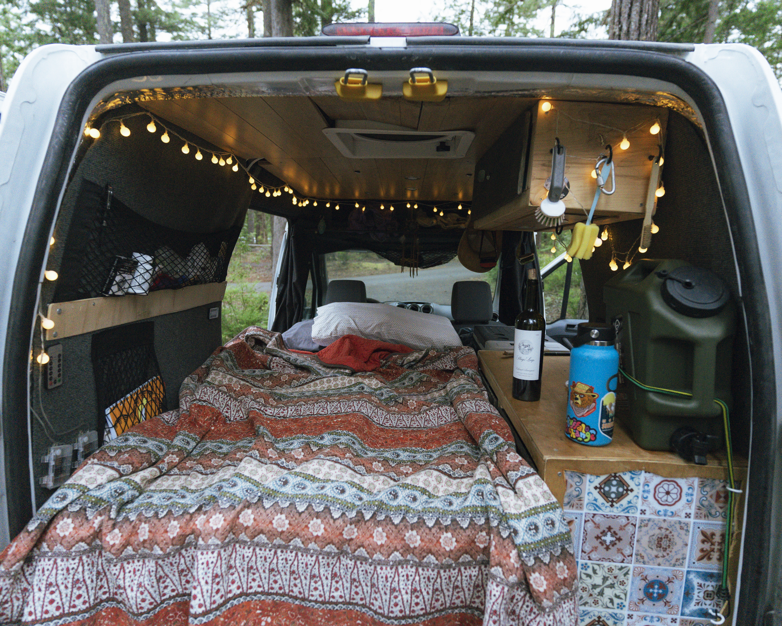 Cozy RV rental interior: a comfortable bed with a patterned blanket, warm string lights, and practical storage solutions.. Ford Transit 2011