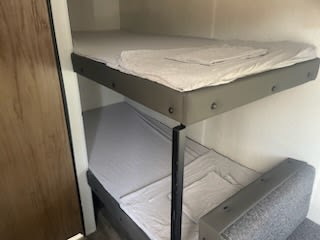 RV rental bunk beds with clean linens. The top bunk is fixed, while the lower converts from a sofa, ideal for family travel.. Forest River Wolf Den 2024